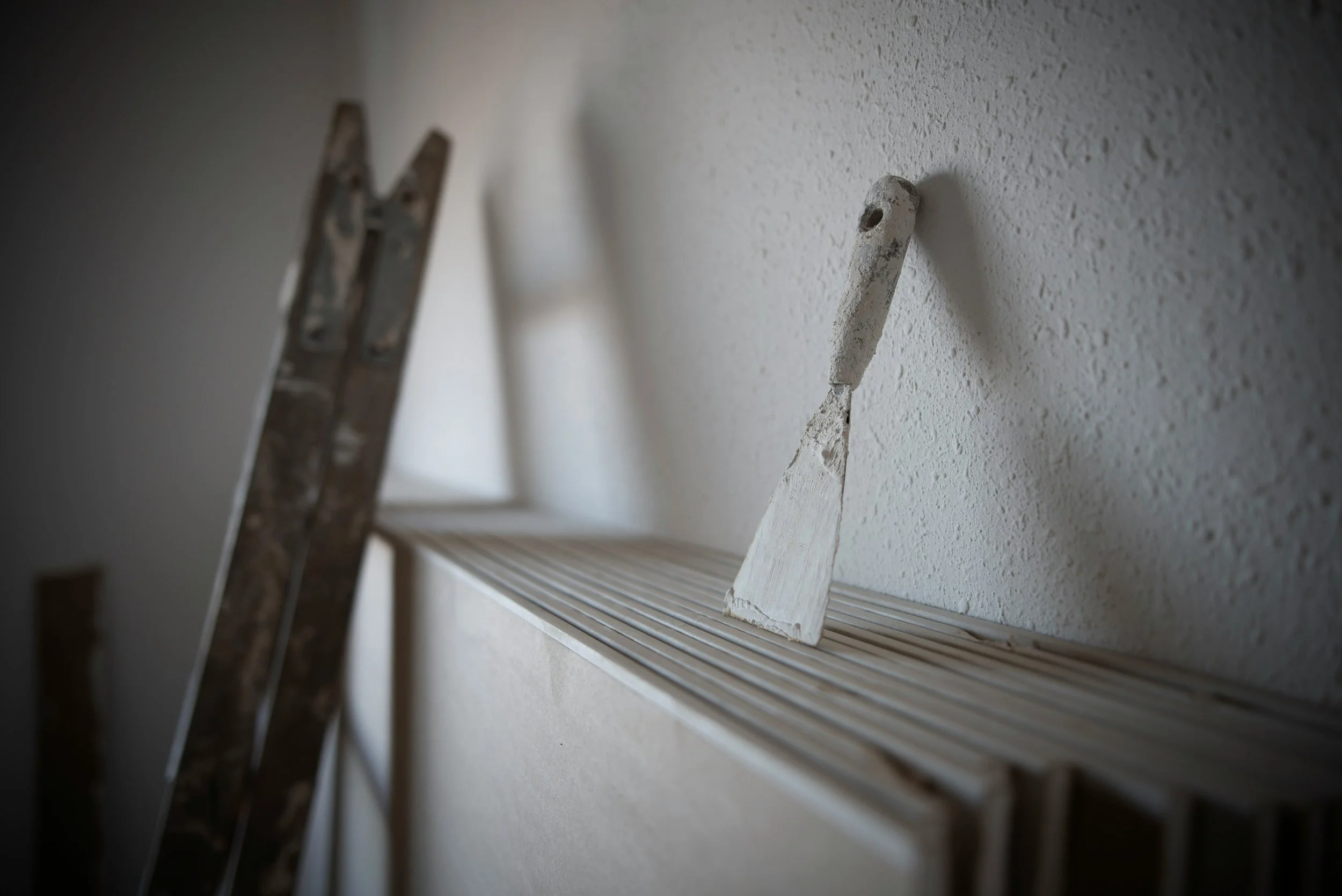 Ladder and wedge on a shelf near a textured wall.
