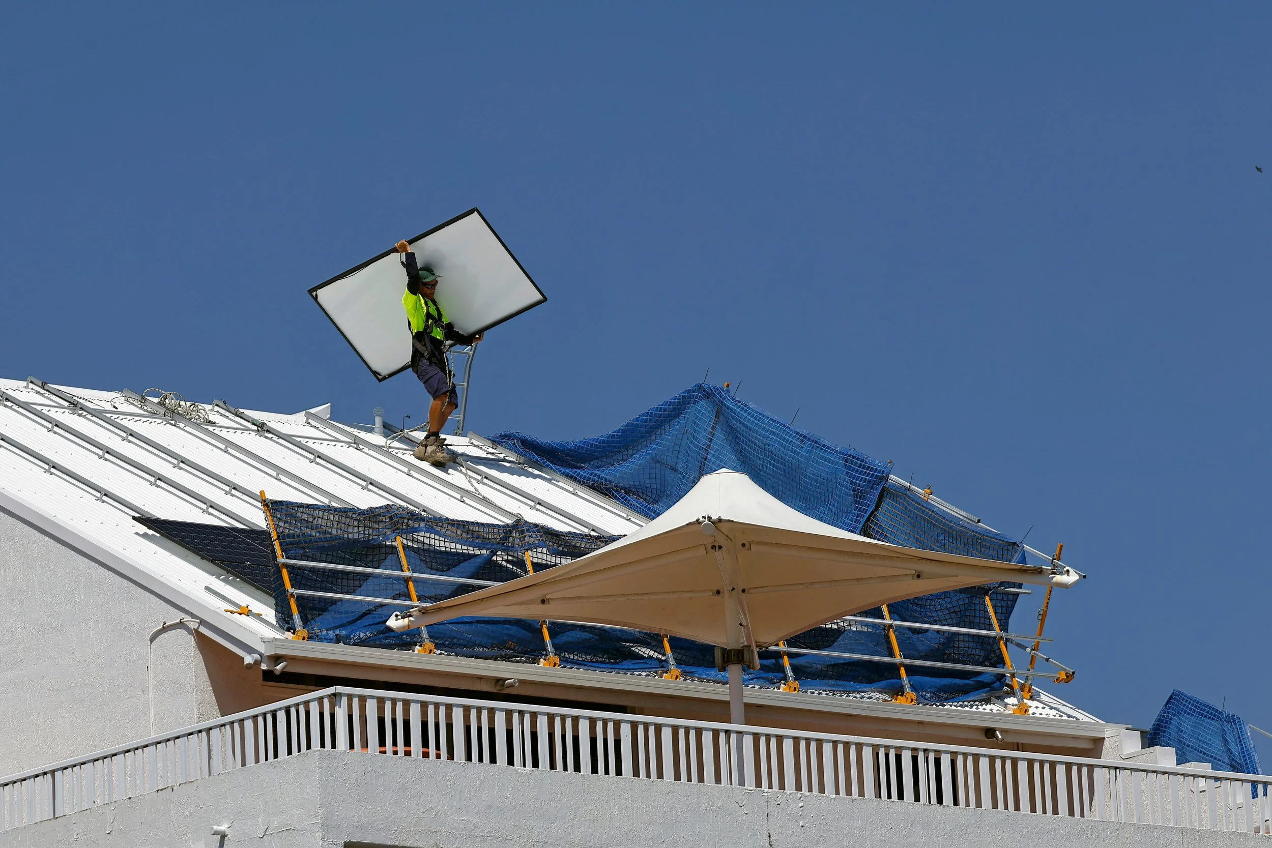 Tradesman on roof carrying solar panels and using safety equipment.
