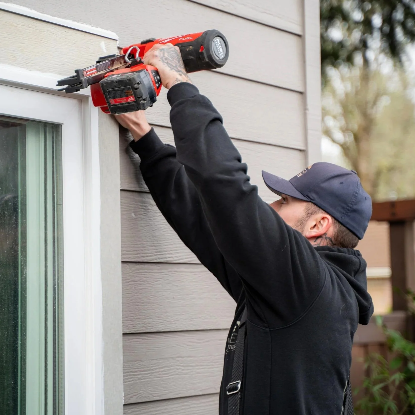 Contractor using power tool to install window trim and siding, demonstrating importance of proper installation for window performance and moisture protection in wet climates.