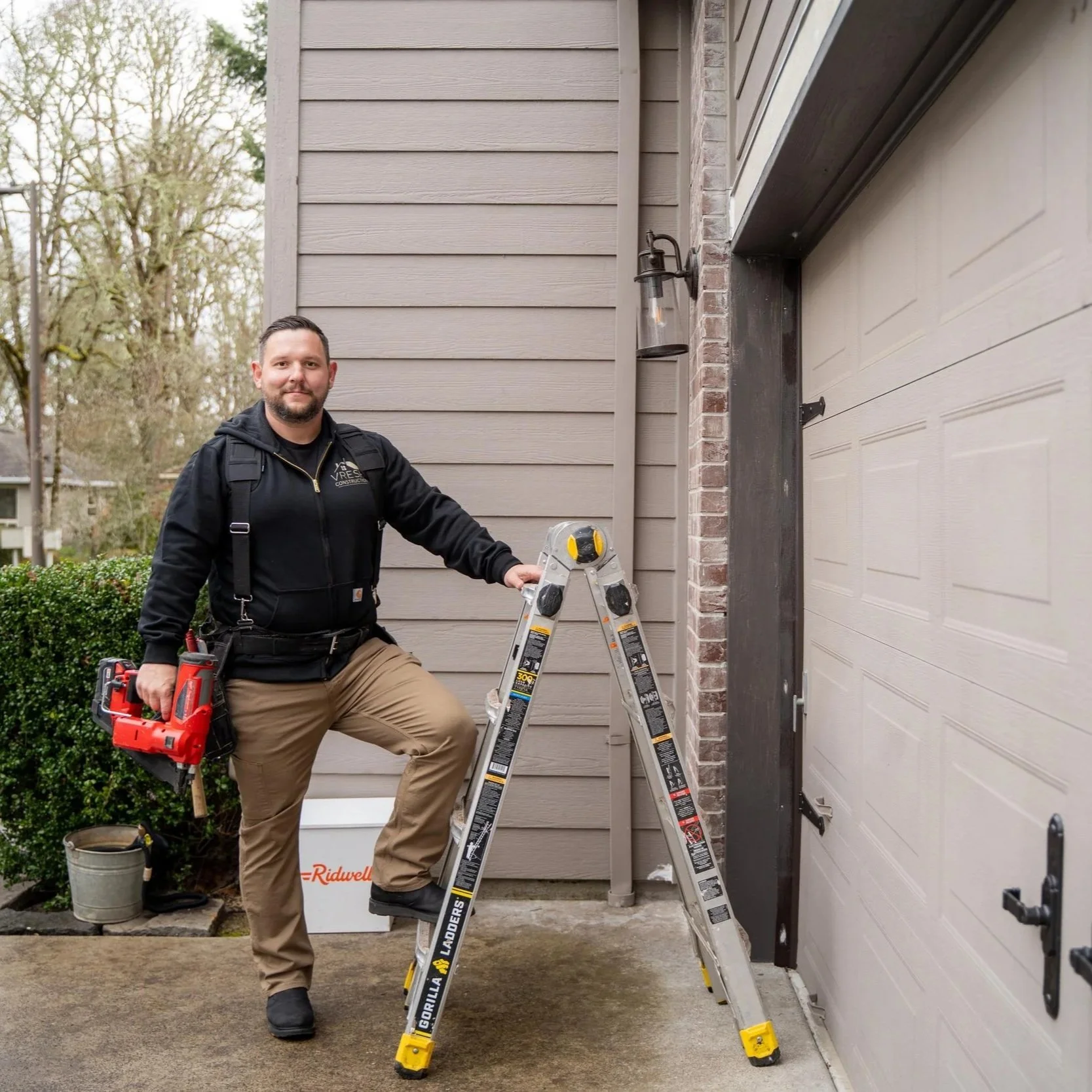 Contractor with tools near home exterior, representing inspection of siding and paint failure causes like moisture intrusion and poor surface preparation in wet climates.