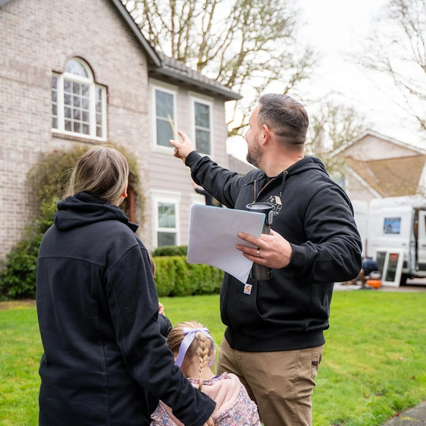 Contractor explaining steel, fiberglass, and wood entry door replacement options to homeowners outside Portland house during renovation consultation meeting.