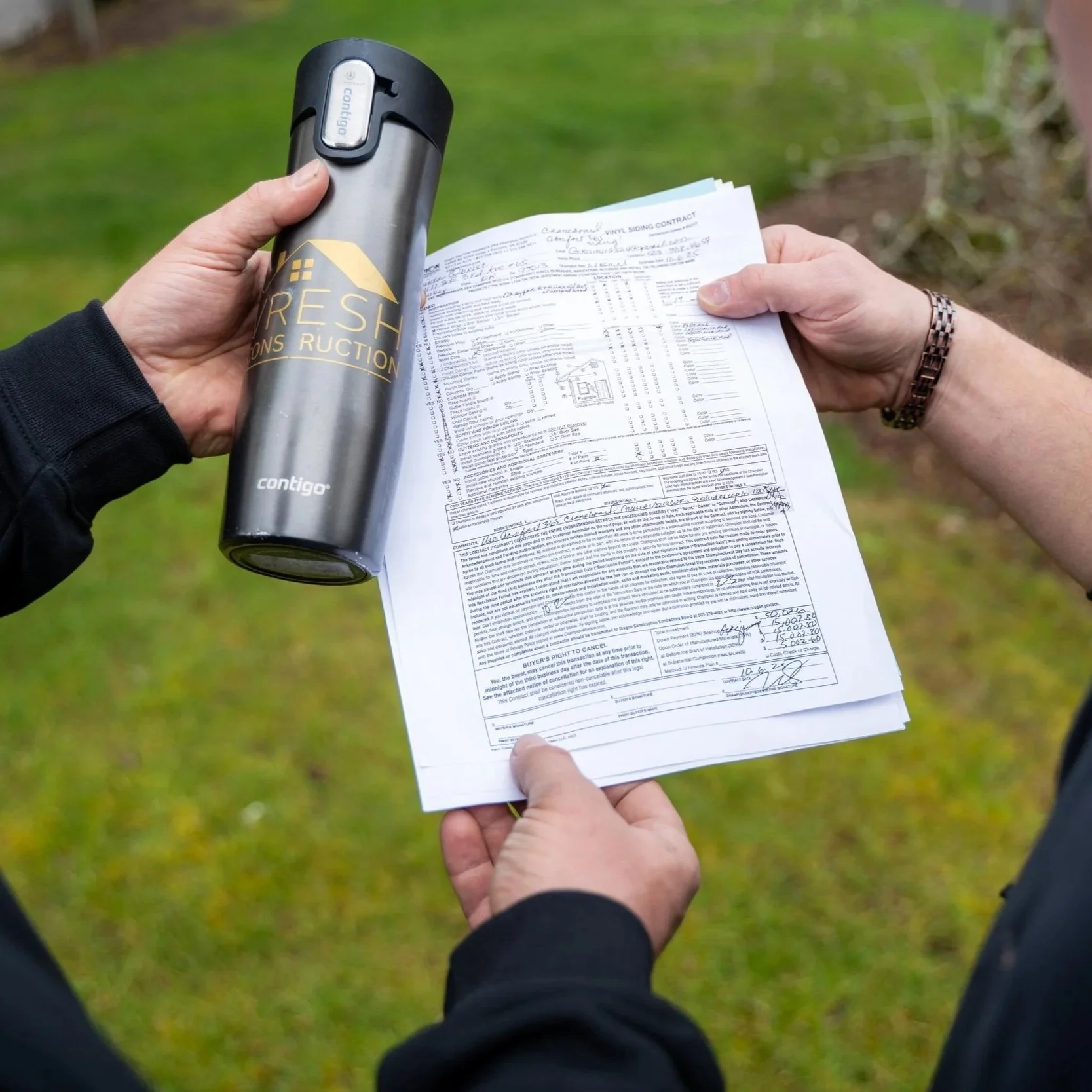 Two contractors examining renovation documents beside insulated bottle while planning Portland kitchen remodel costs, plumbing repairs, and electrical upgrades.