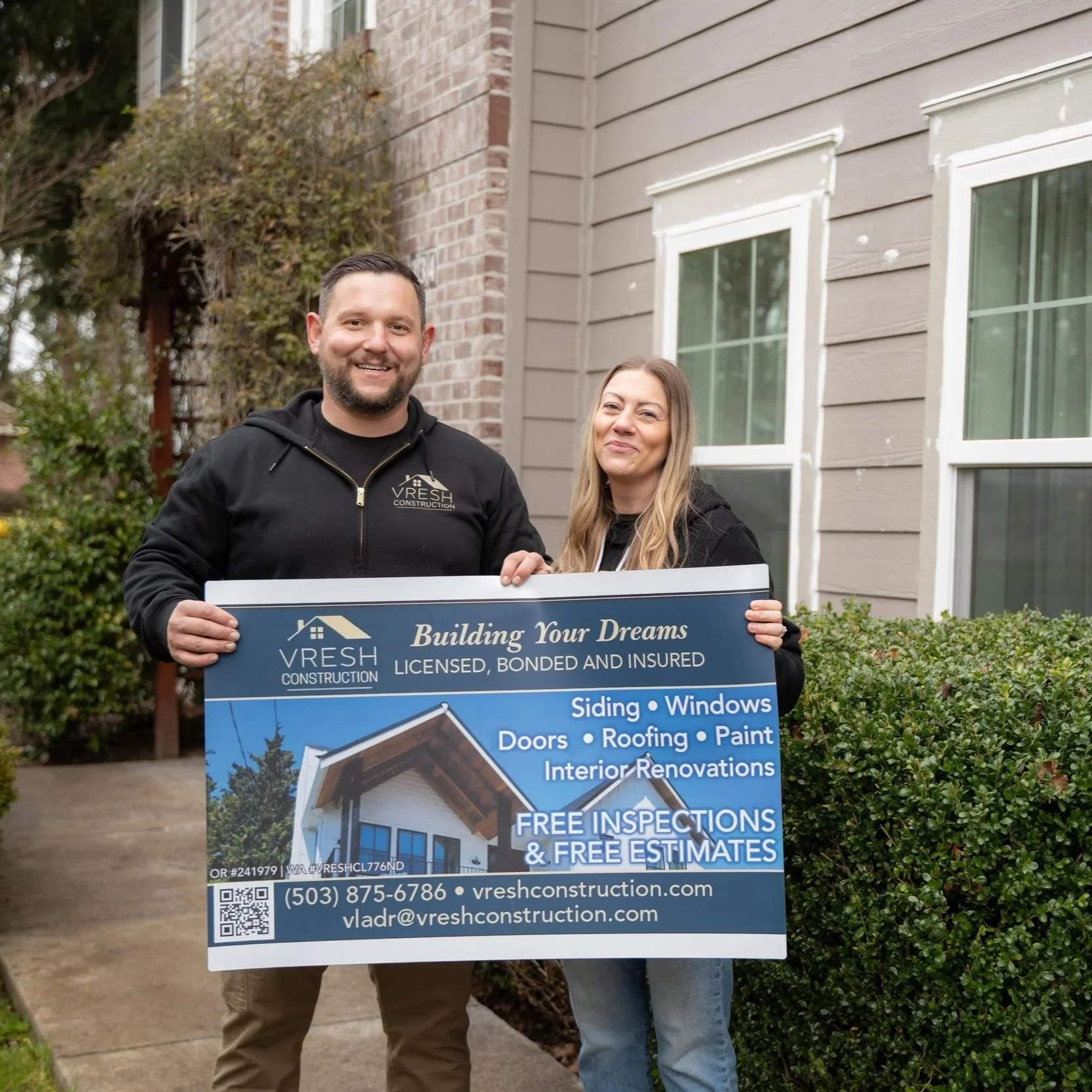 Homeowners and contractor holding project sign in front of house, representing importance of hiring experienced professionals for historic home renovations and preservation work.