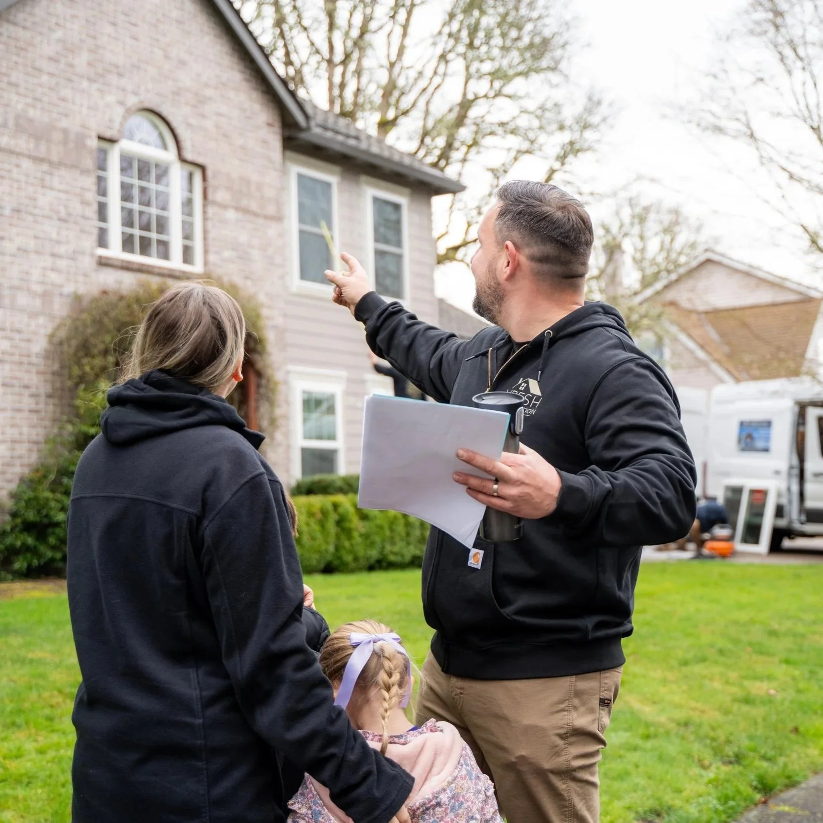 Contractor pointing at house roof while speaking with homeowner, indicating inspection of roof condition and planning for Malarkey shingle replacement in Portland.