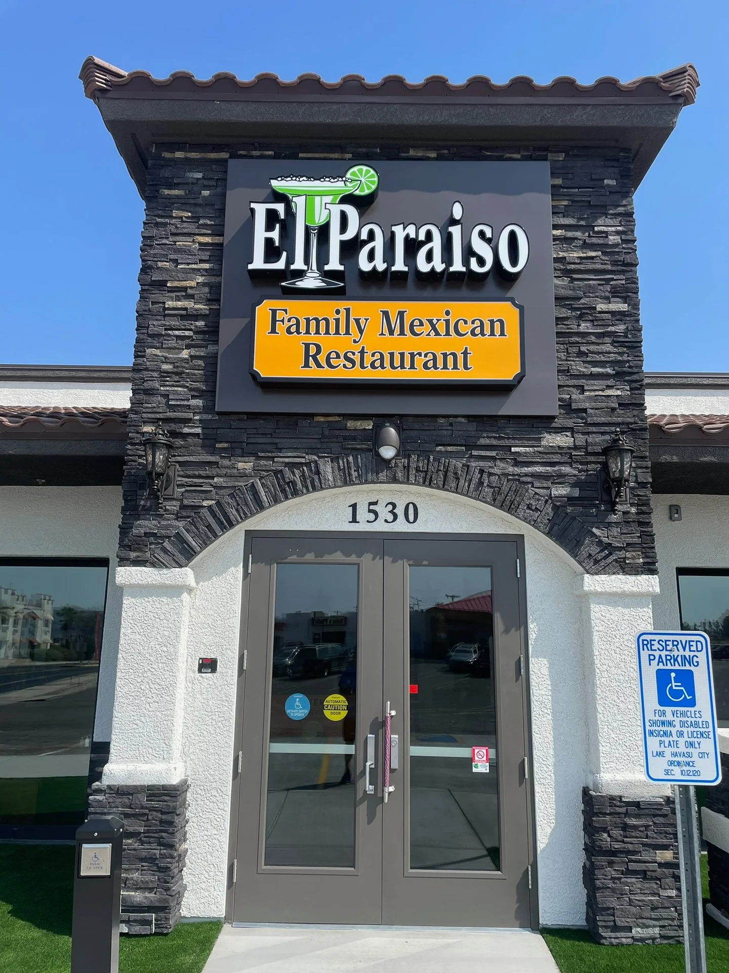The entrance of El Paraiso family Mexican restaurant with sign above the door and reserved parking sign on the right.