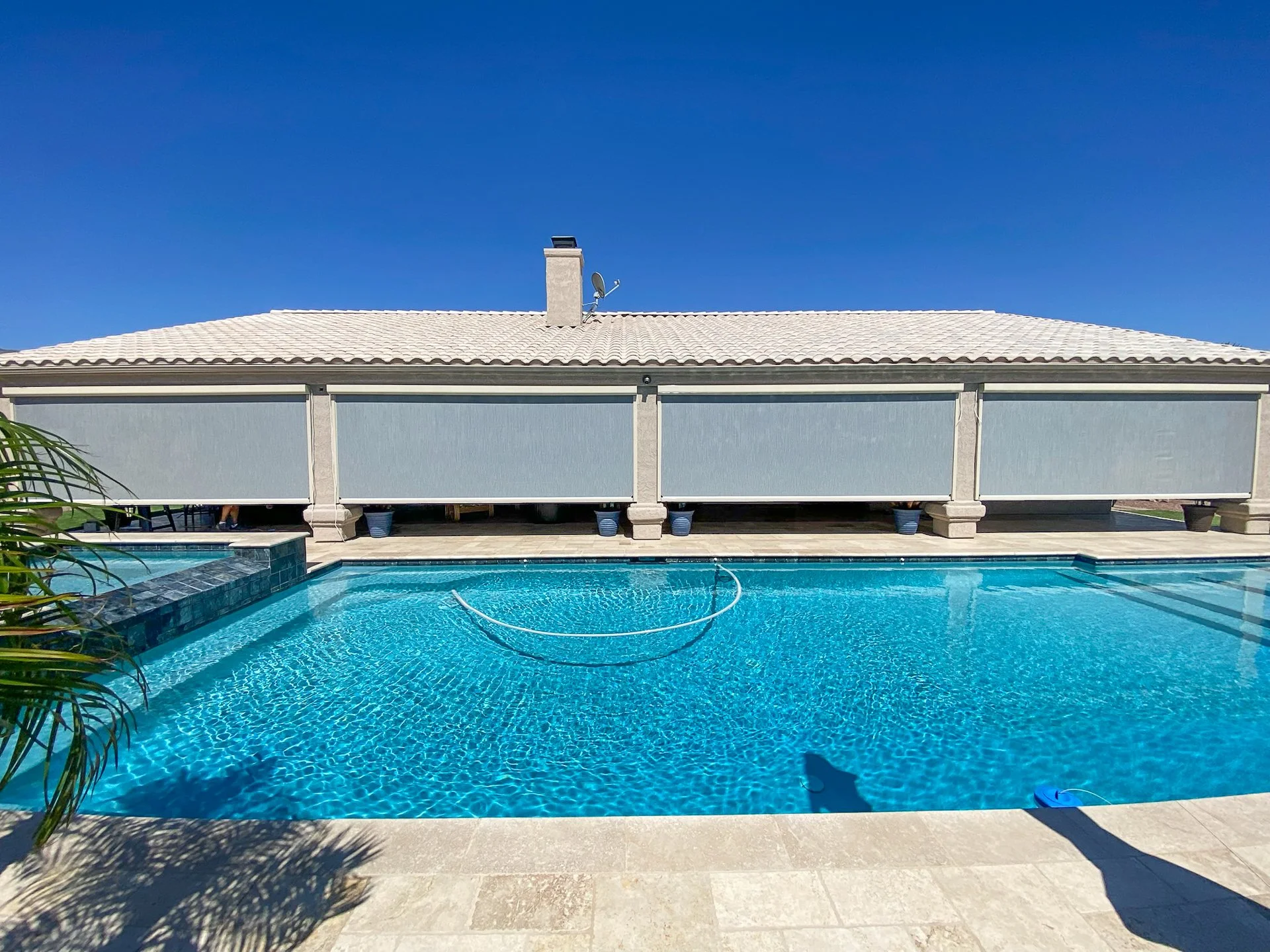 Swimming pool with a house or building behind, blue sky, shadow of a plant in the foreground.