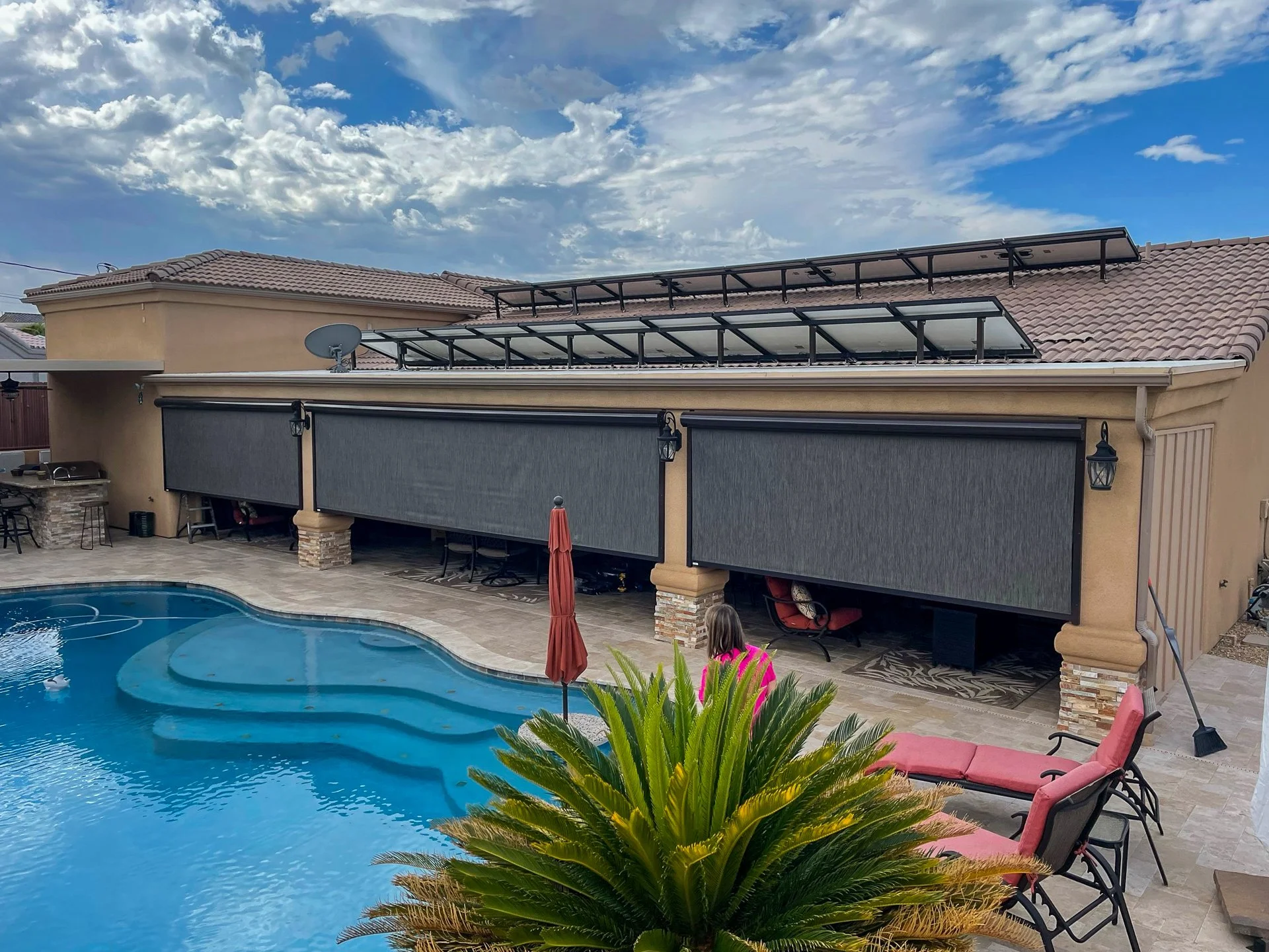 A backyard with a swimming pool, outdoor furniture, and a house with solar panels and roll-up screens.
