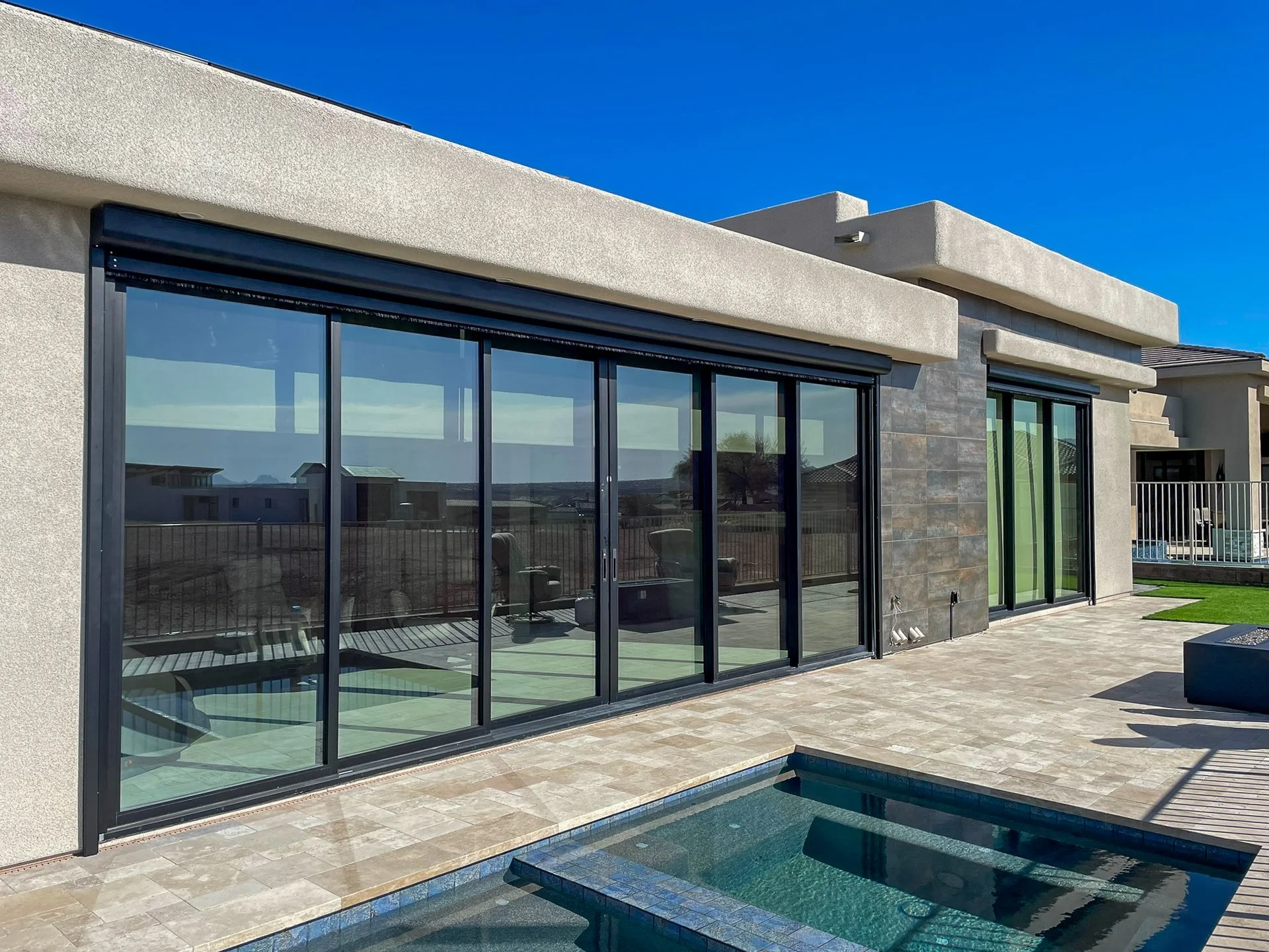 Modern house with large glass sliding doors, a small pool, and outdoor patio area during daytime.