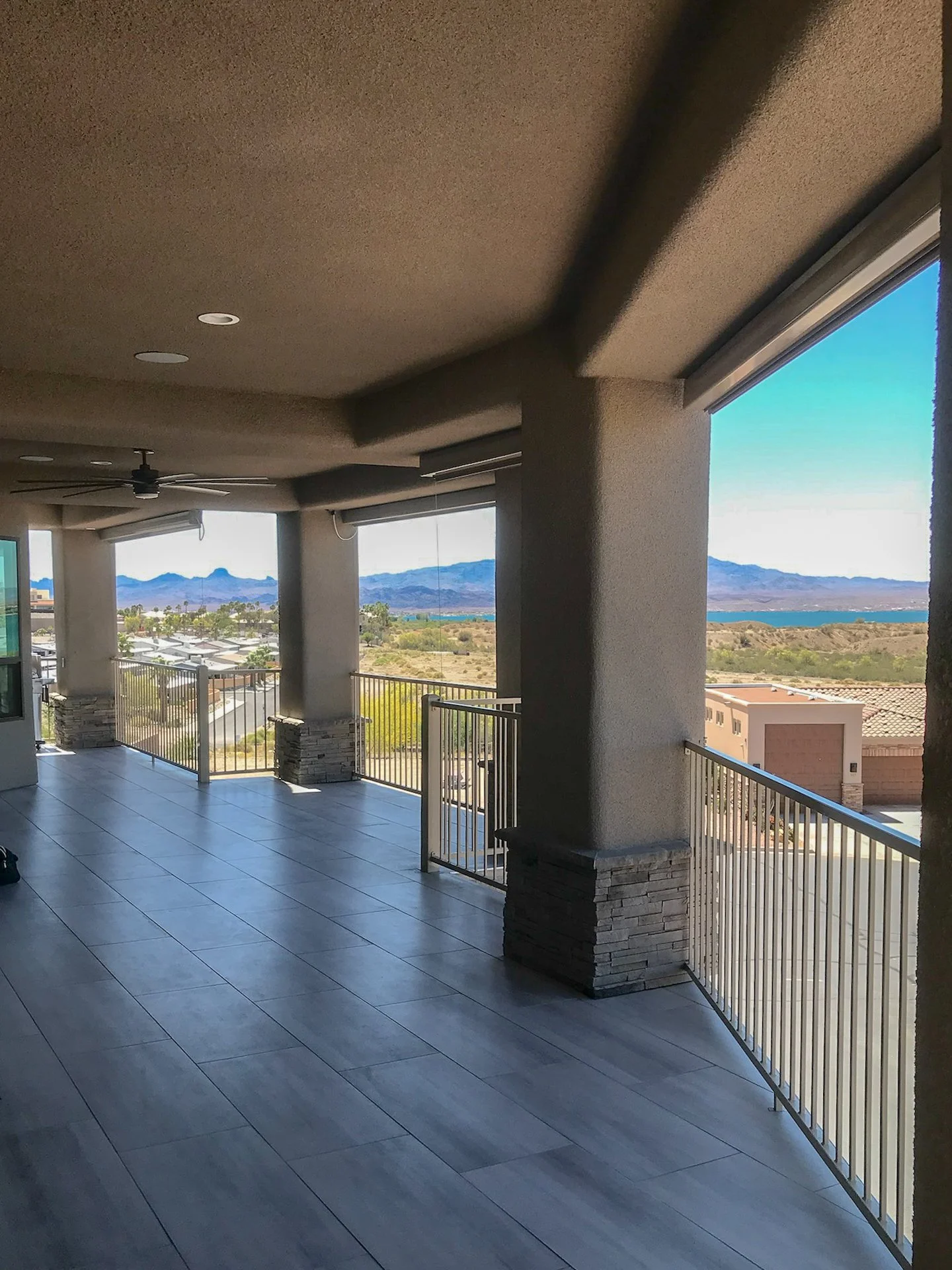 Indoor balcony area with large open windows showing a desert landscape, mountains, and a body of water in the background.