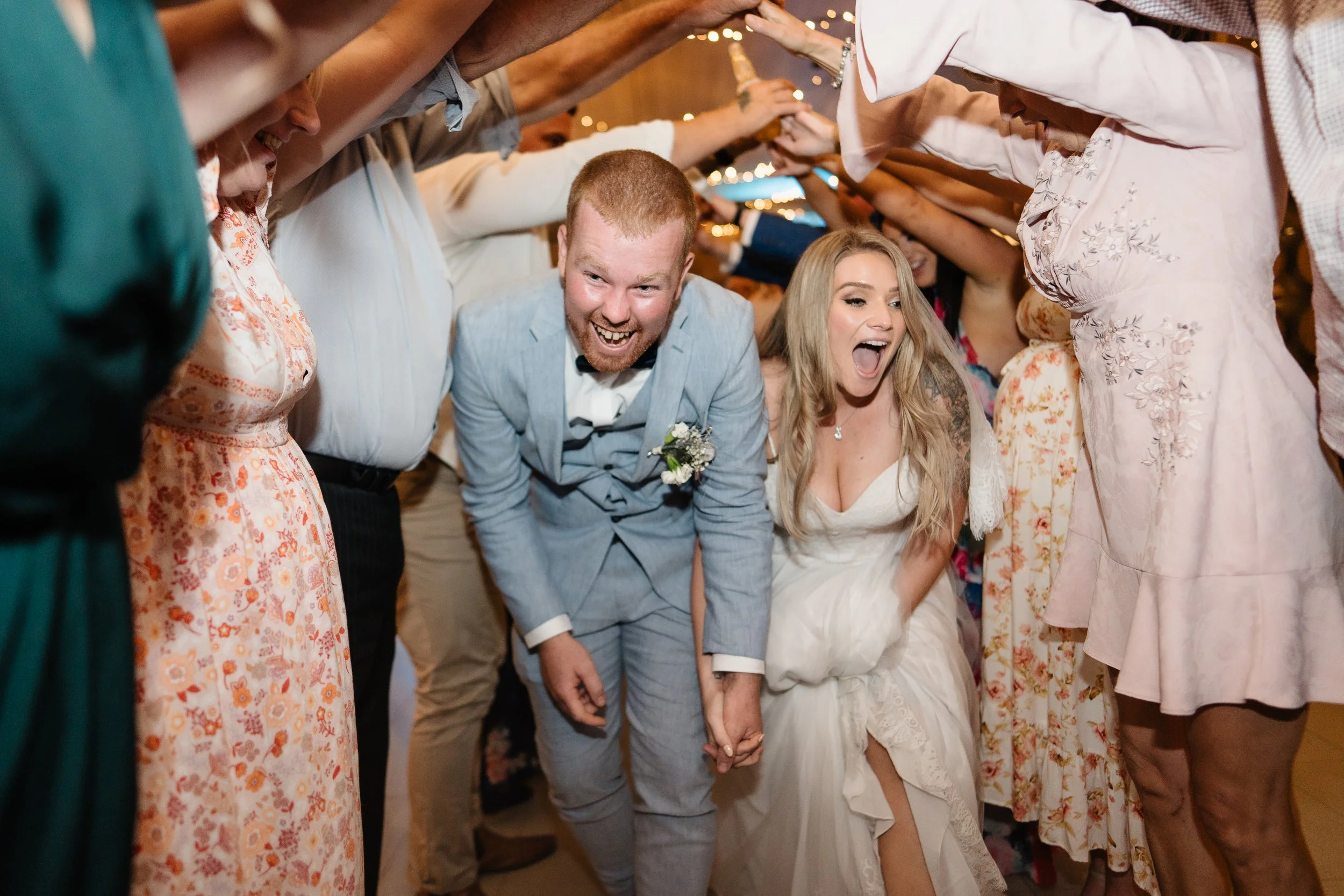 A bride and groom at their wedding reception holding hands and smiling as they walk through a tunnel of guests.