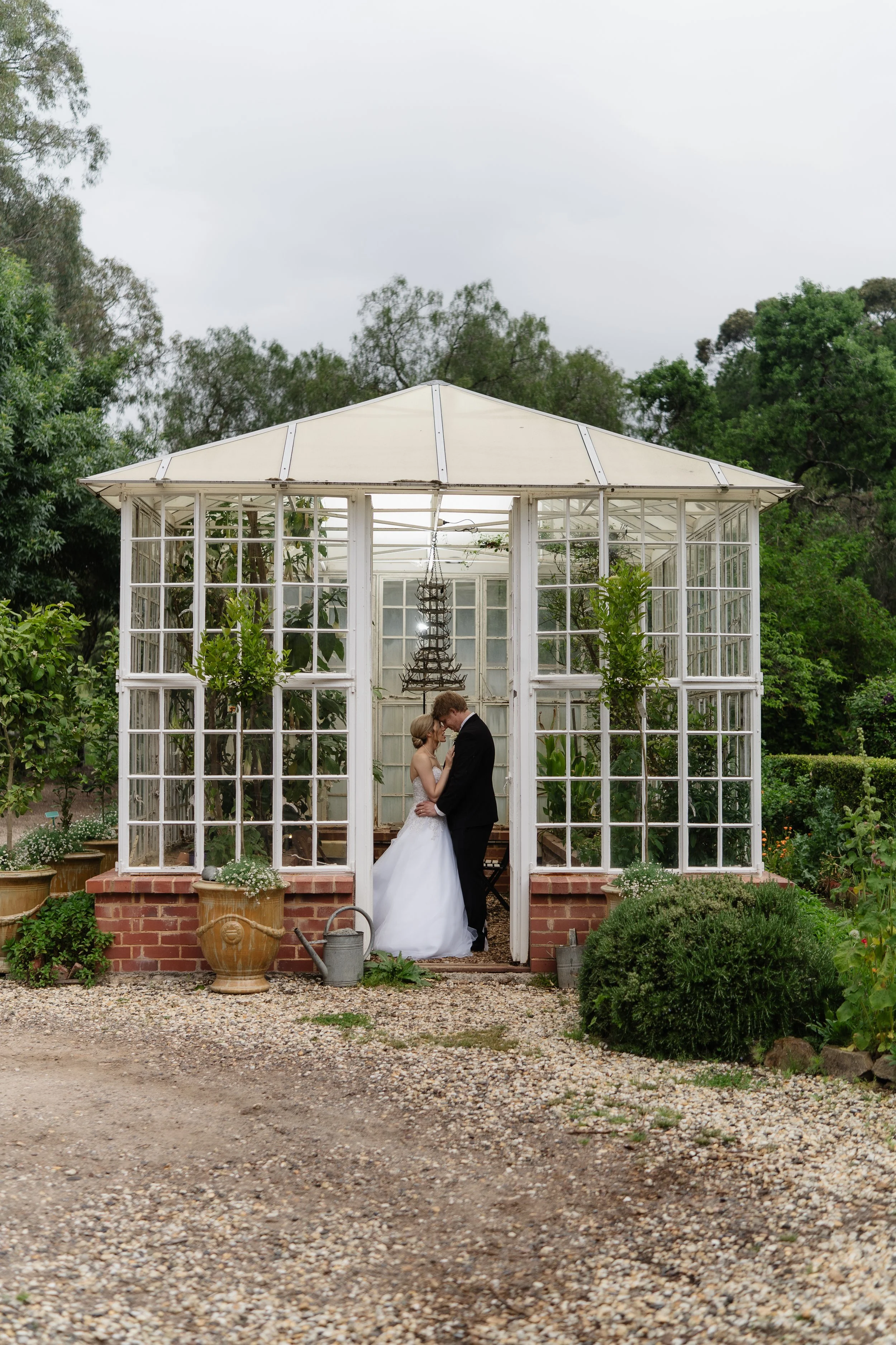 Bride and groom embracing in the glasshouse garden at Al Ru Farm, a popular Adelaide Hills wedding venue.