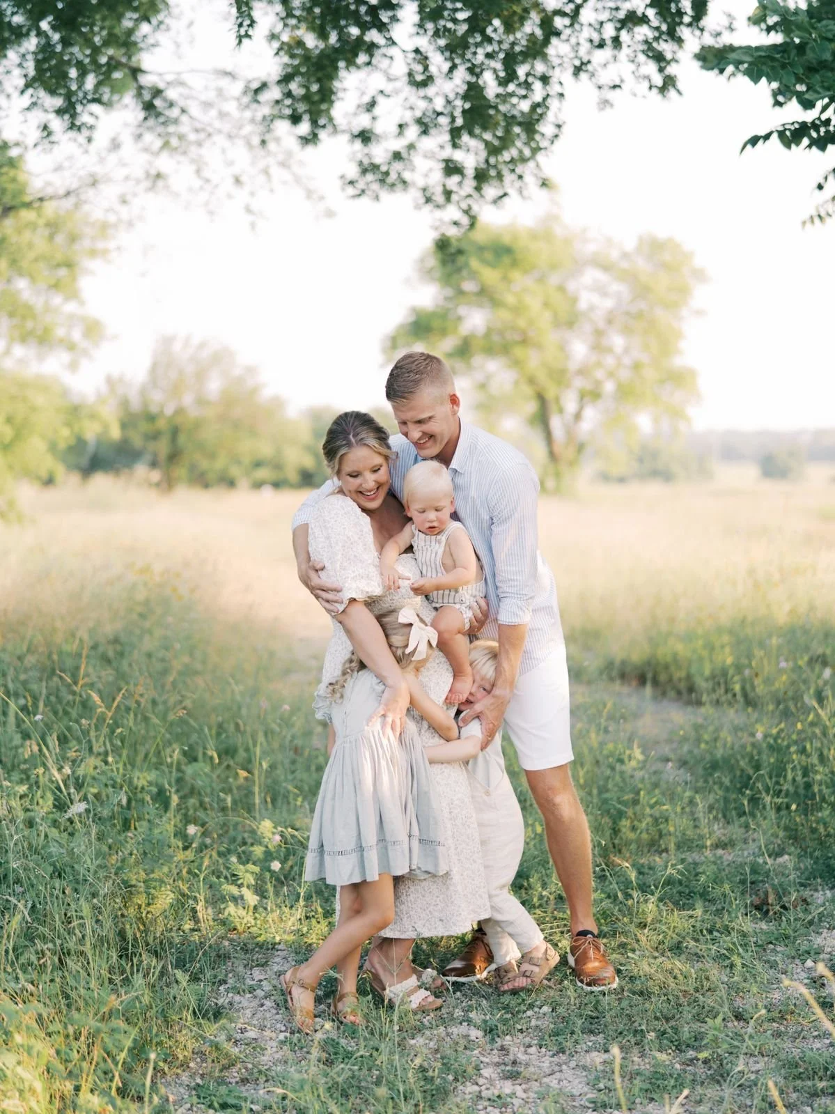 A happy family of five, including two adults and three children, enjoying an outdoor moment in a green field on a sunny day.