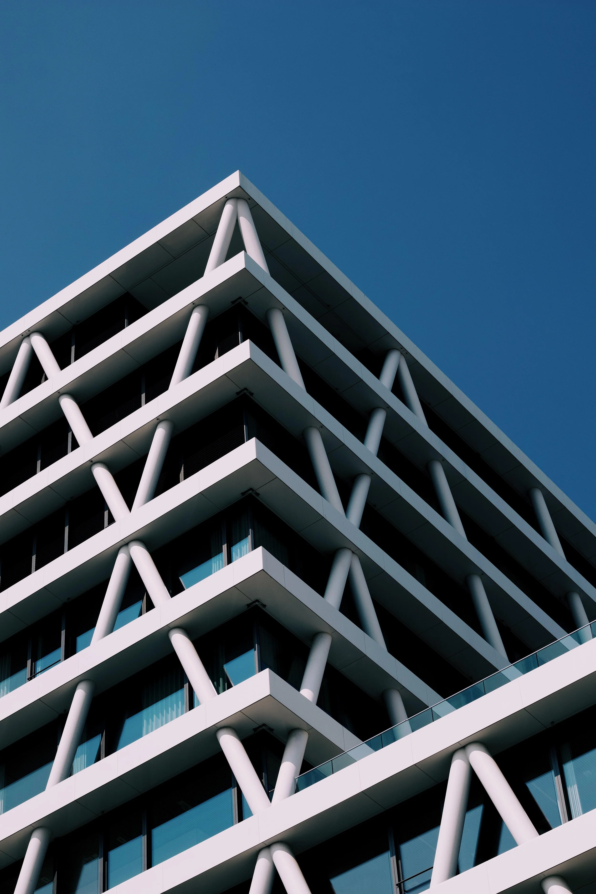 Modern multi-story building with geometric architecture, white structural beams, and large glass windows against blue sky.