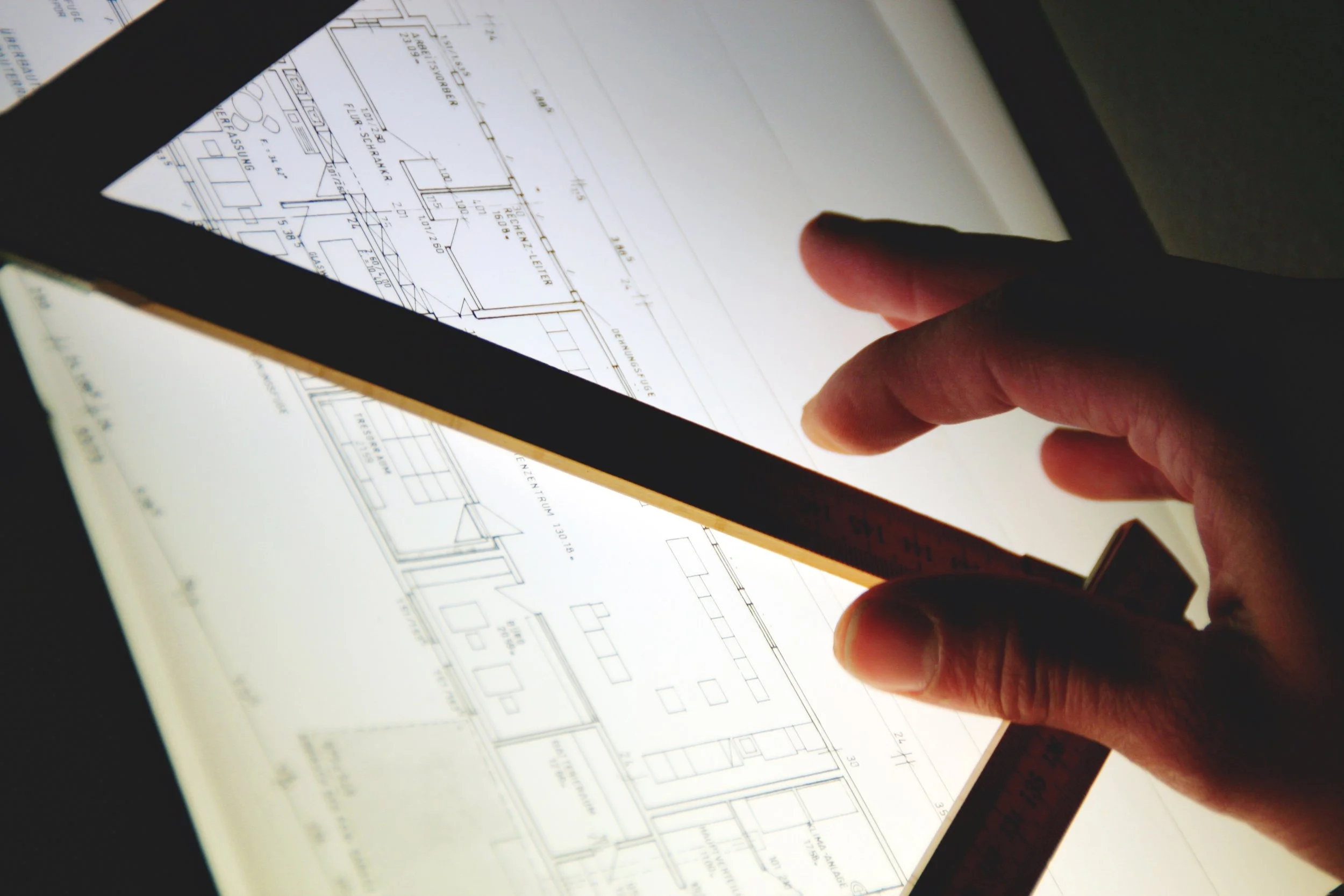 Person using a ruler and touching a digital blueprint or architectural plan on a tablet or computer screen.