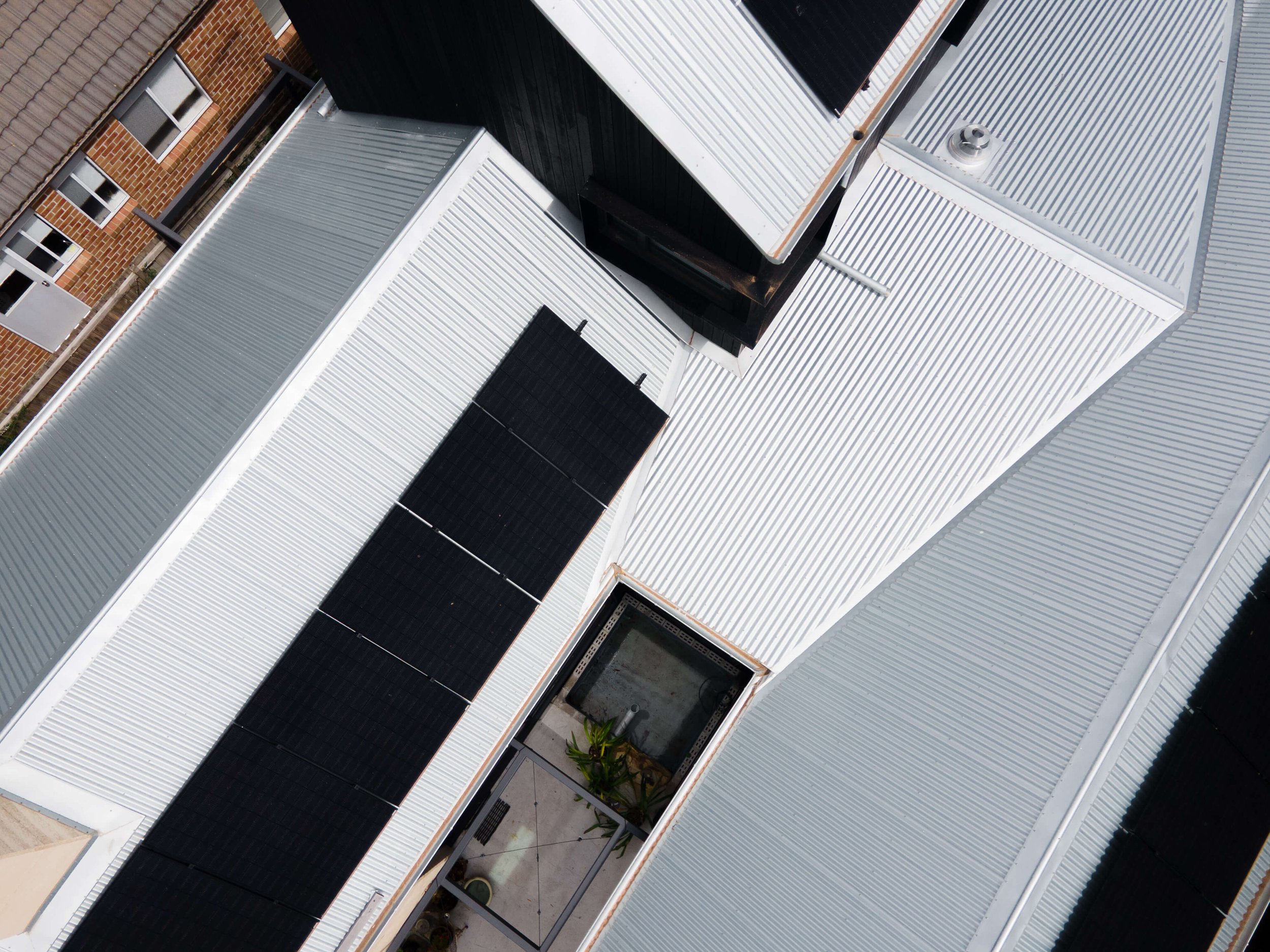 Overhead view of residential rooftops with metal roofing, vents, and a small area with plants and a plant stand.