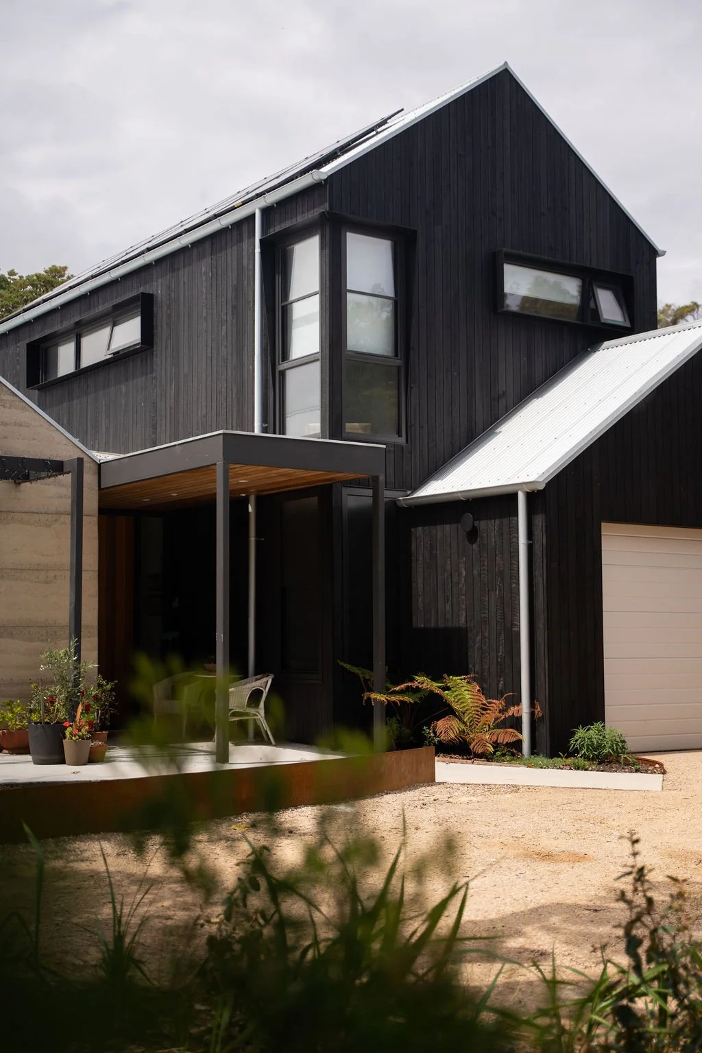 Modern black house with unique angled windows, a metal roof, and a small outdoor seating area with plants