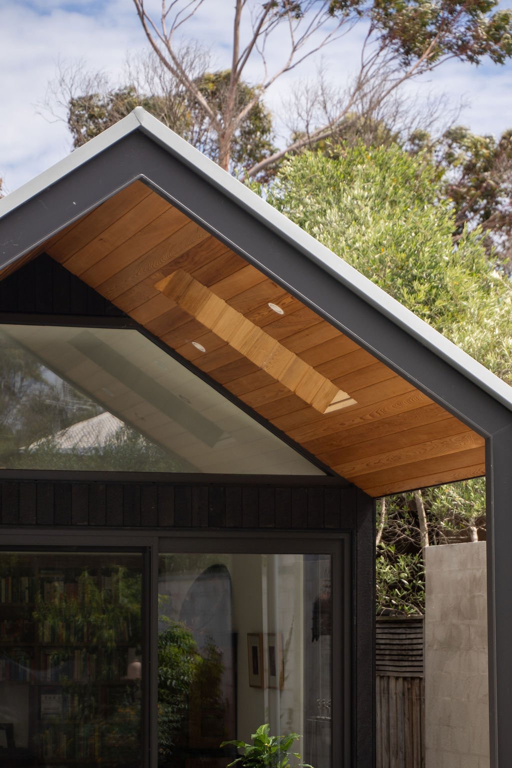 Close-up of a modern house's roof with metal flashing and wooden soffit, with trees in the background.