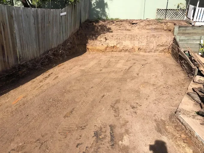 Empty backyard with cleared dirt ground, surrounded by a wooden fence and partial house exterior.