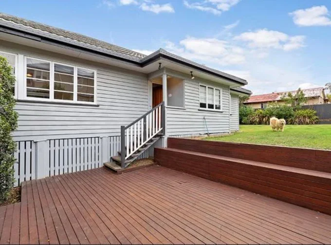 Backyard with a spacious wooden deck, small stairs leading to a grassy area with a dog, and a white house with sliding windows.