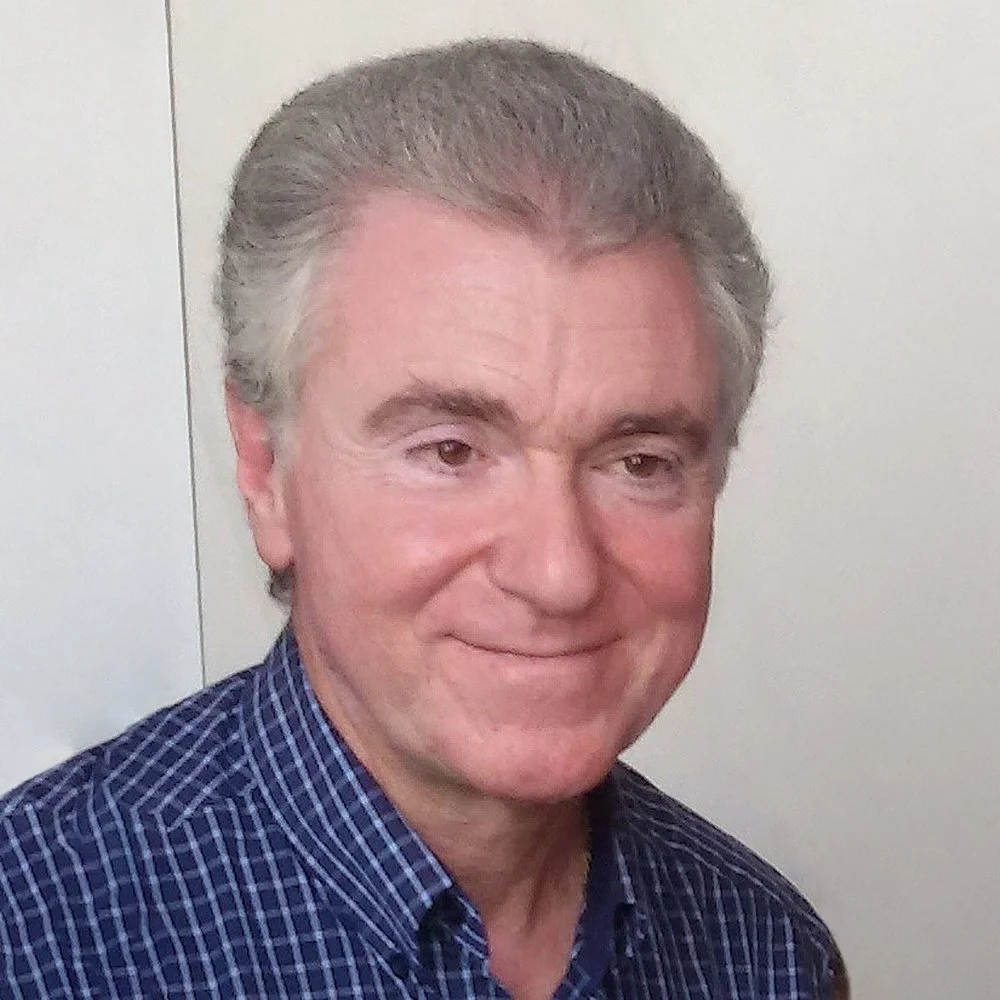 A middle-aged man with gray hair and a blue checkered shirt smiling at the camera.