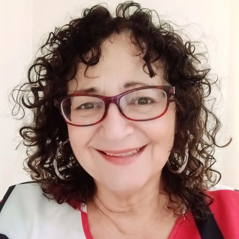 Close-up photo of a smiling woman with curly hair wearing glasses and a red and white top.