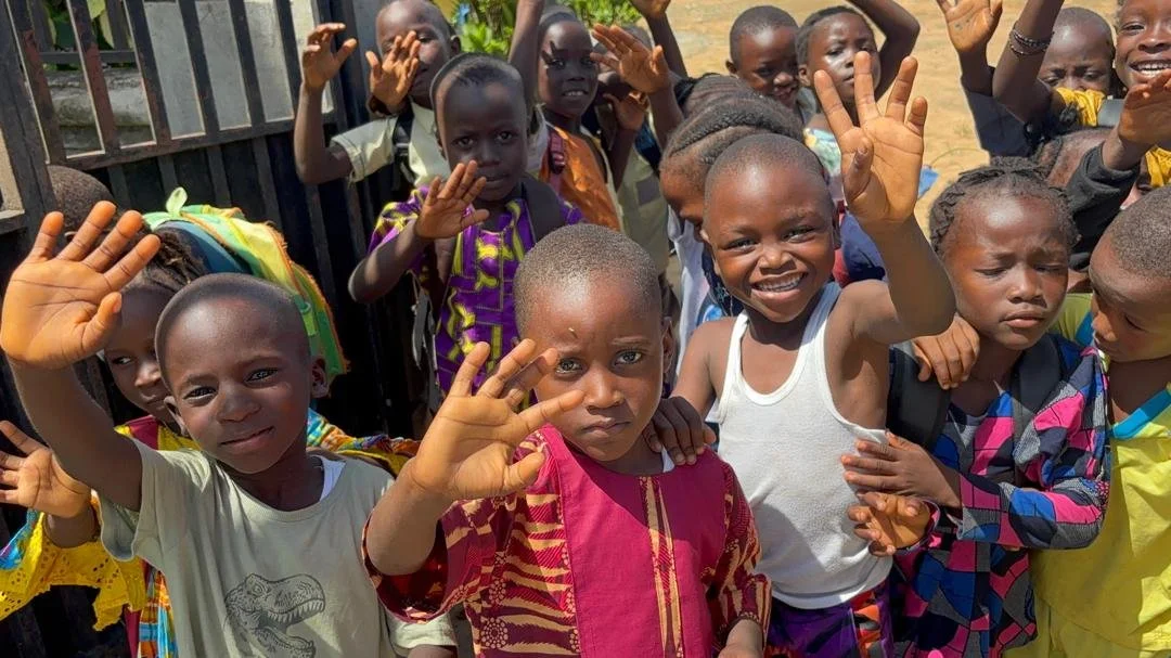 Group of smiling African children waving at the camera outdoors.