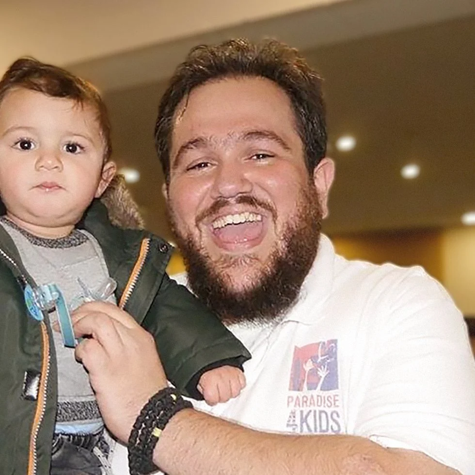 A smiling man holding a young child in an indoor setting with warm lighting.