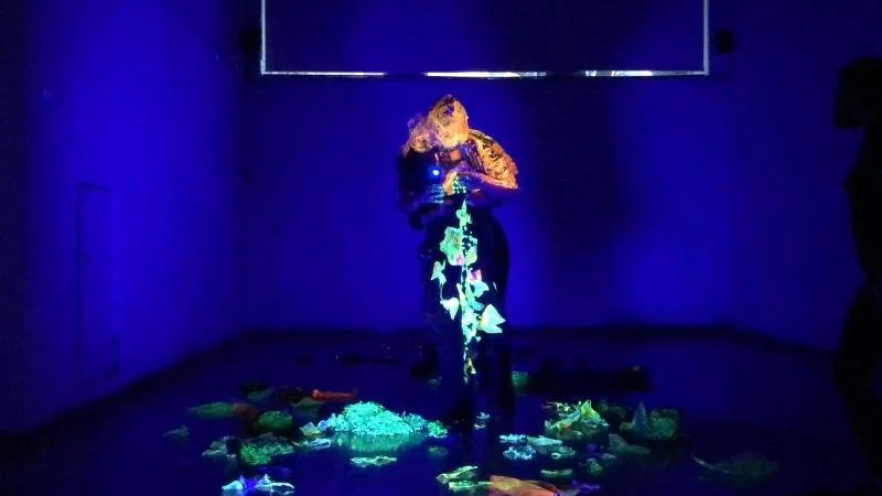 Persona interactuando con una obra de arte luminosa en una sala oscura.