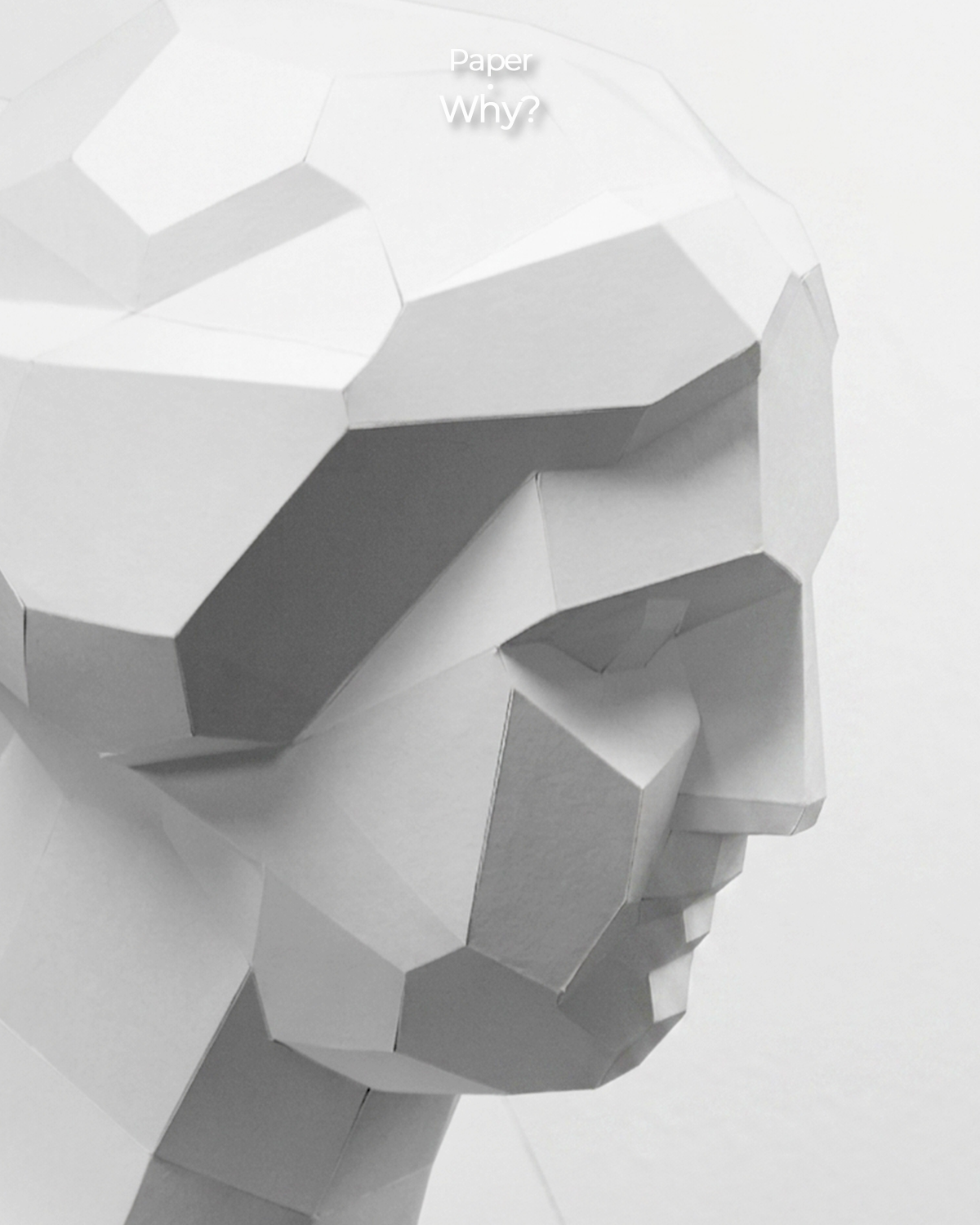 Close-up of a white low-poly paper sculpture of a classical face, revealing geometric planes and sharp contrasts of light and shadow.  Copy
