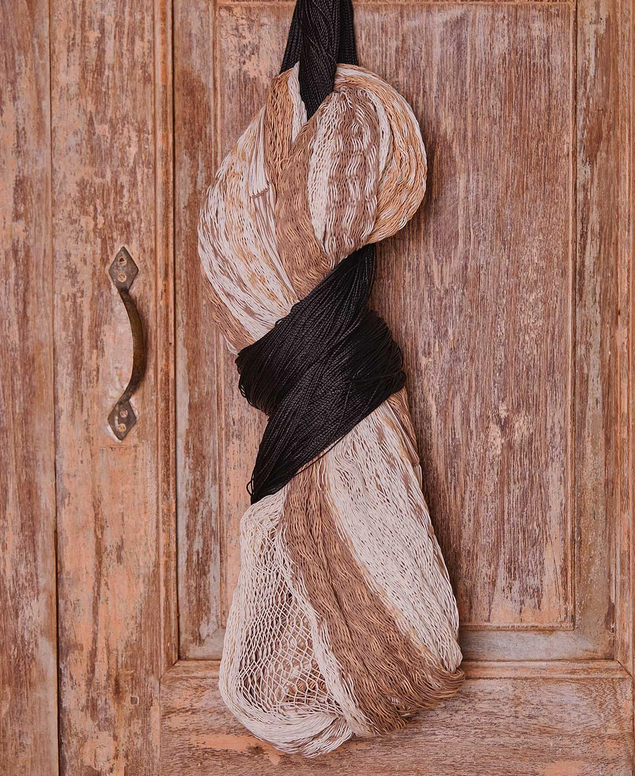 A bundle of rolled-up black, white, and beige yarns or knitting supplies hanging on a rustic wooden door with a metal handle.