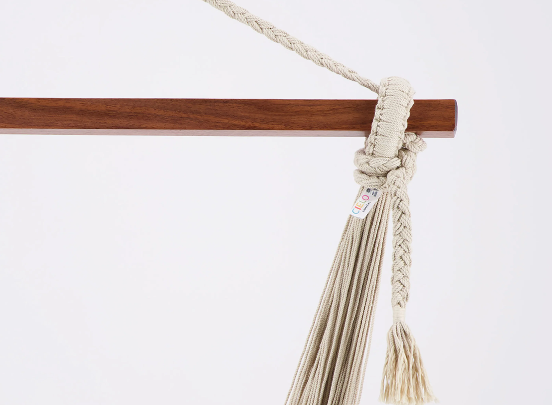 A hanging macrame plant holder with a wooden bar and beige cord.
