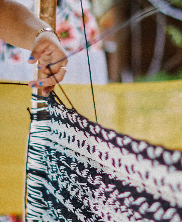 A person's hand with painted nails is seen adjusting a piece of black and white woven fabric on a loom.