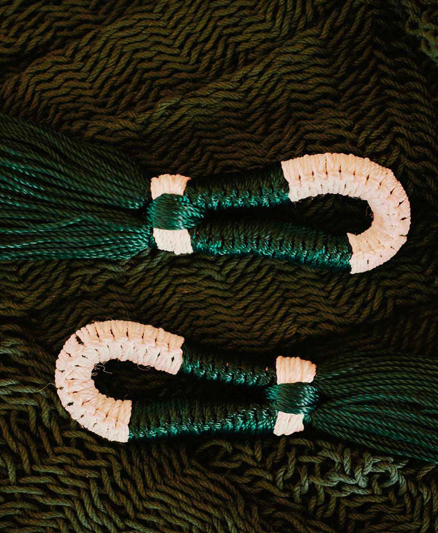 Two bundles of dark green embroidery floss wrapped around white plastic or bone floss bobbins, lying on a dark textured fabric background.