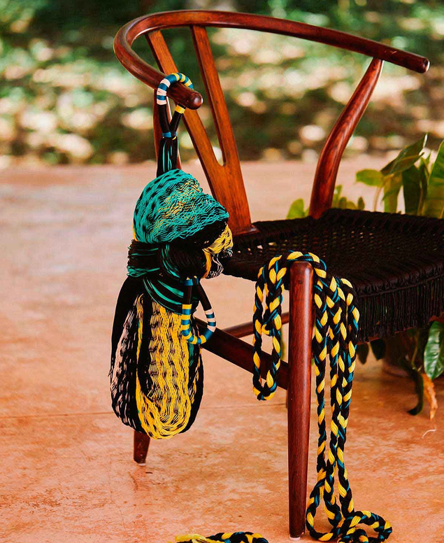 Colorful yarns and scarves draped over a wooden chair on a porch, with a plant nearby.