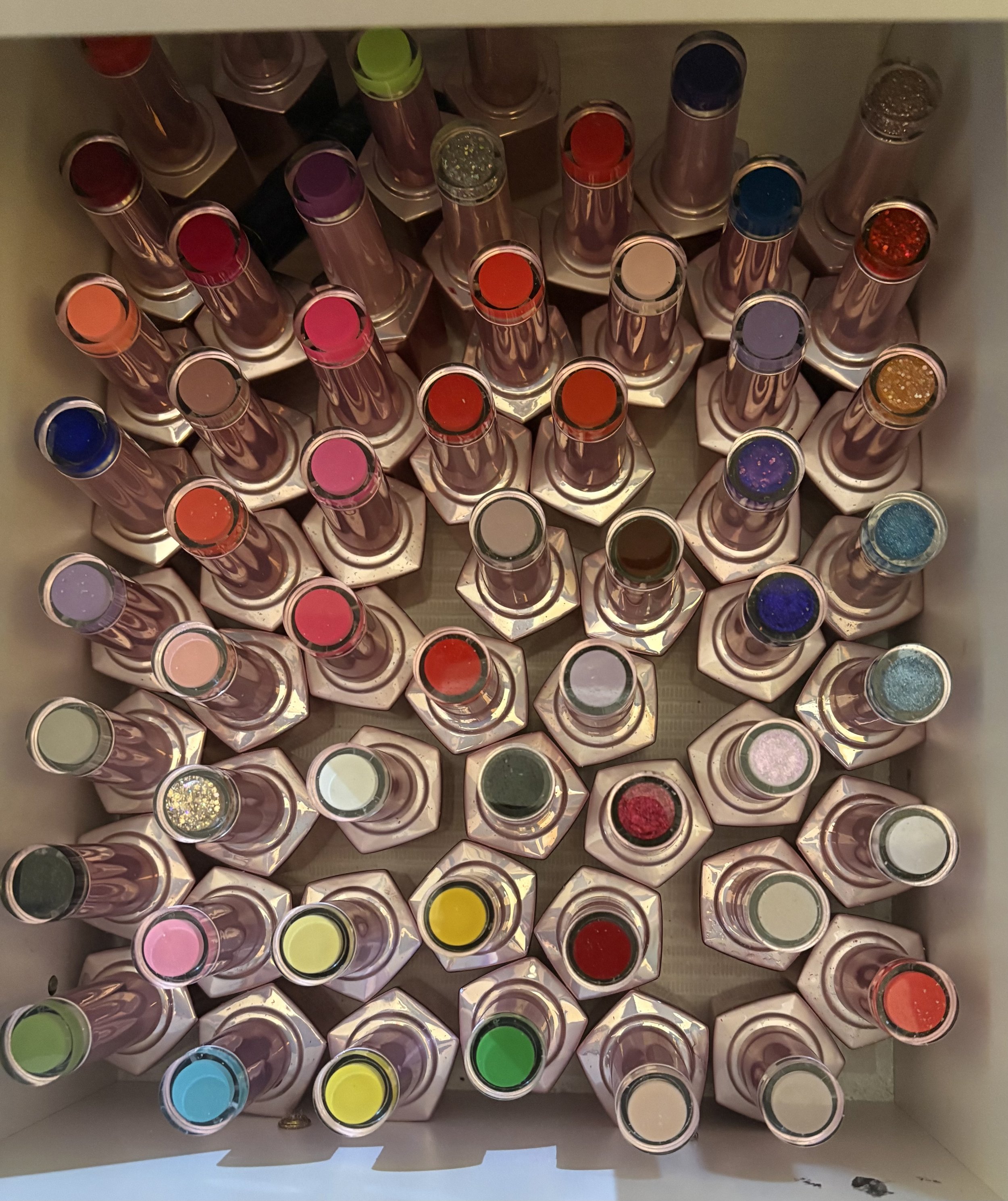 Top view of a box filled with various colorful lipstick tubes with different caps, arranged in neat rows.