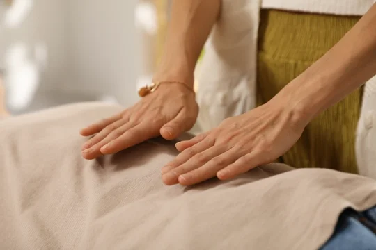 A ladies hand held over a person laying on a therapy couch, giving Reiki Healing.