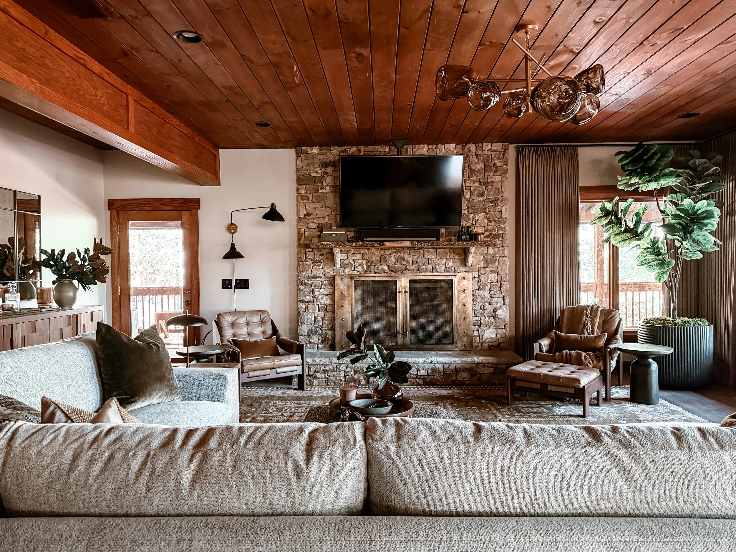 Mountain lodge style living room with stone fireplace, leather seating, and layered materials designed by Studio Meadow in North Georgia