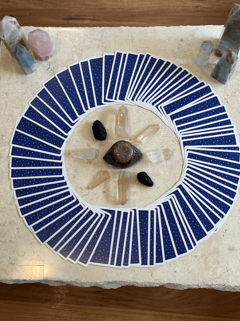 A fan of tarot cards arranged in a circle on a stone surface, with various crystals placed in the center and around the circle.