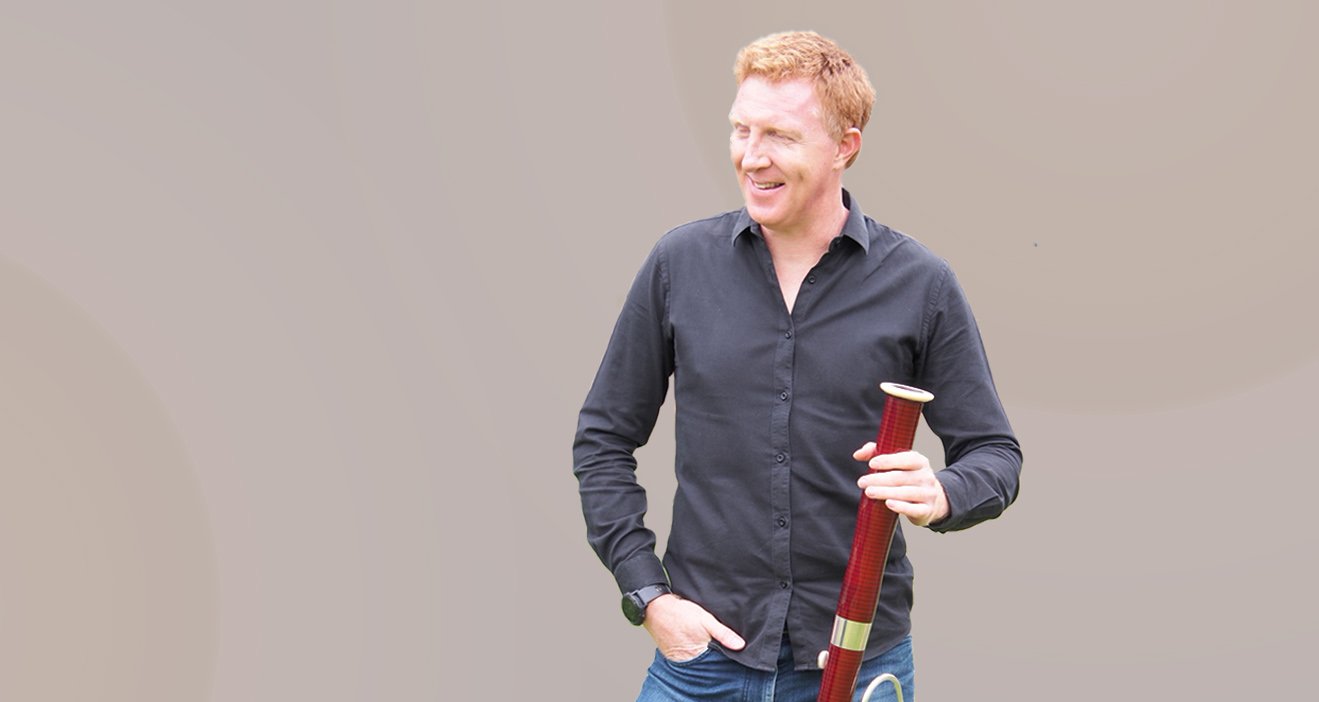 Matthew Angus professional bassoonist holding bassoon bell looking away from the camera smiling