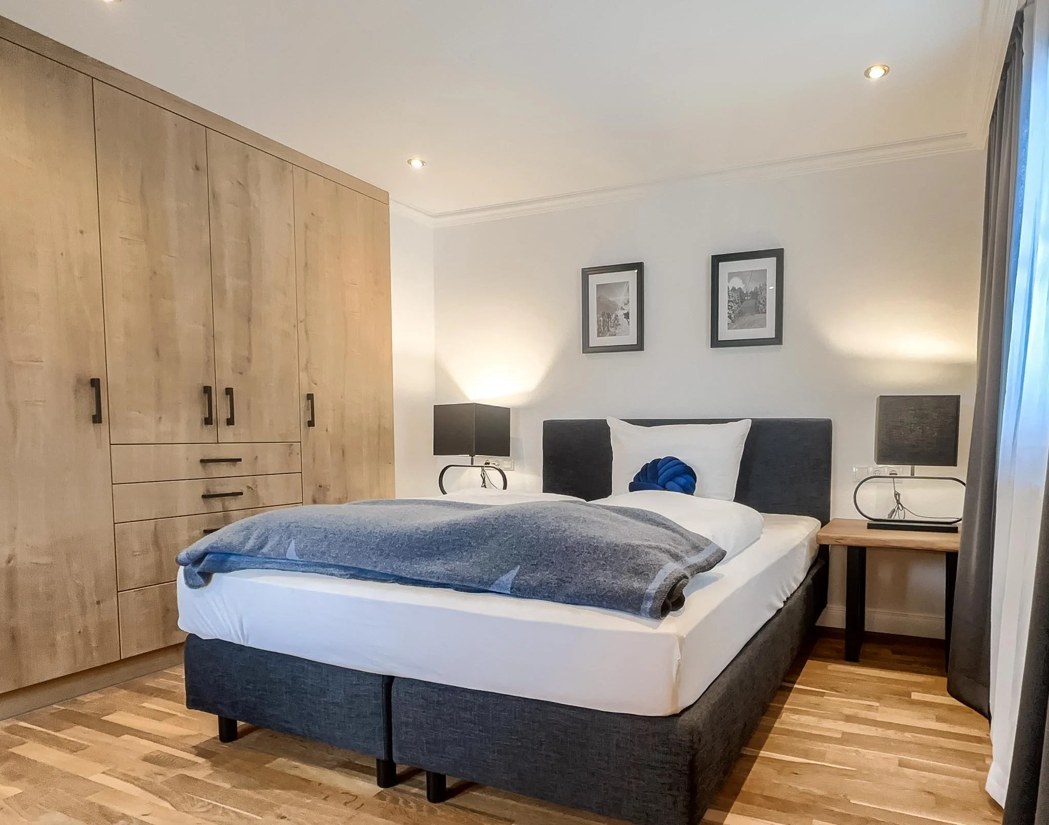 Schlafzimmer mit Doppelbett, Nachttischen, Lampen, Wandbildern und einem großen Kleiderschrank aus Holz.