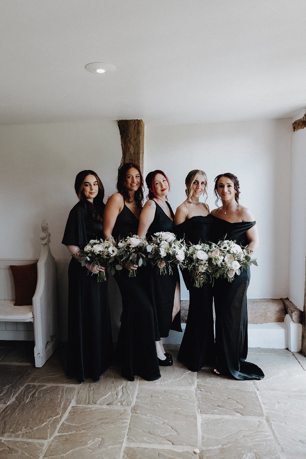 Bridal party wearing black grouped together smiling at camera holding wedding bouquets