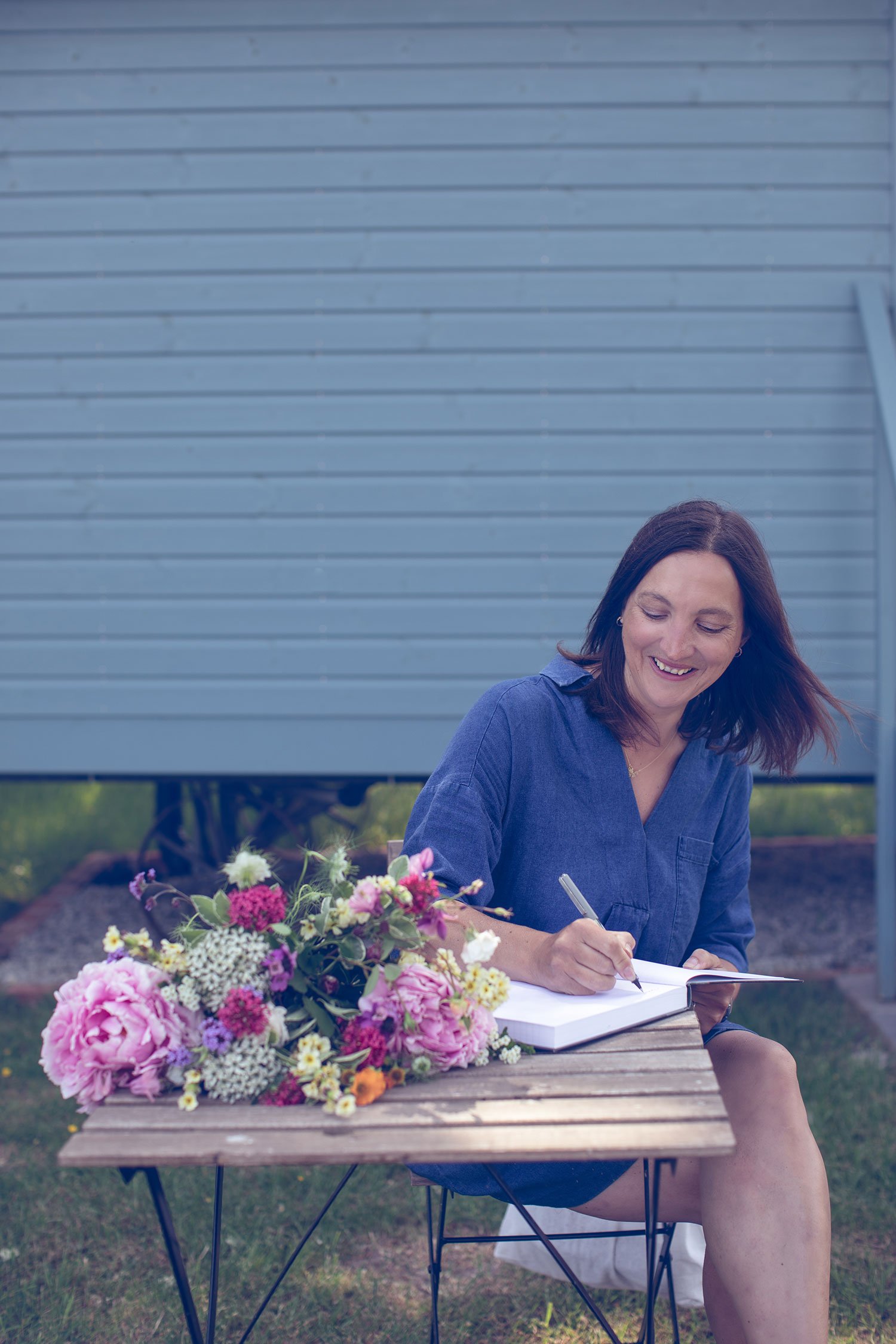 Kent and London based wedding florist sat outside writing at table with blooms