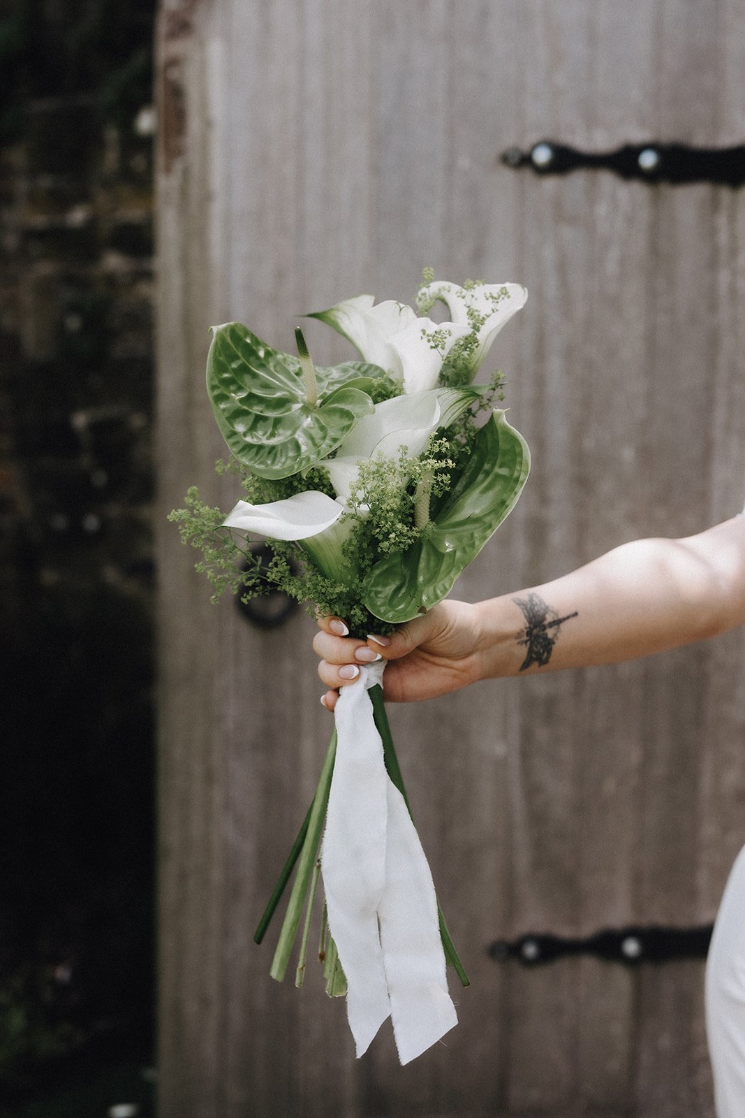 Bride holding wedding bouquet to one side with green botanical calla lily arrangement