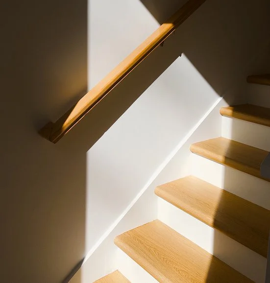 Wooden stairs with sunlight casting shadows on the white wall beside them.