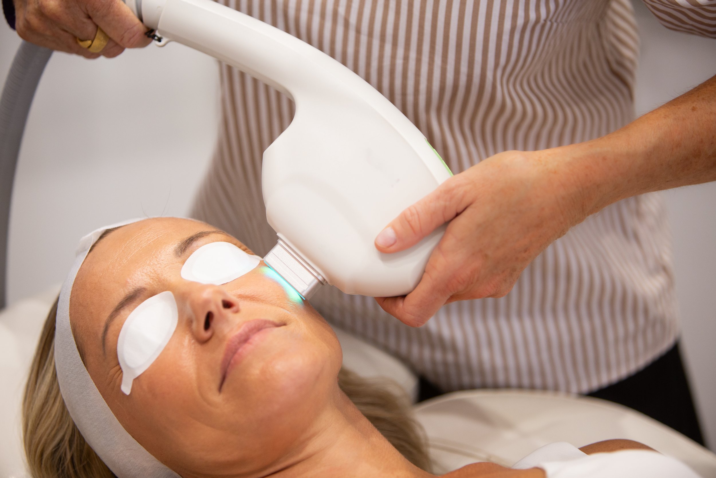 A woman receiving a facial treatment with a laser device at a skincare clinic.