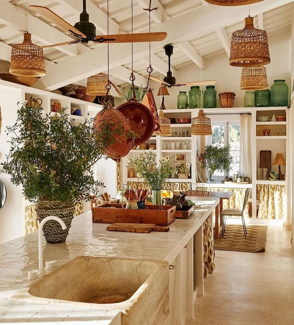 Bright kitchen and dining area with white cabinetry, hanging woven pendant lights, green jars on the shelves, and a large potted plant on the island countertop.