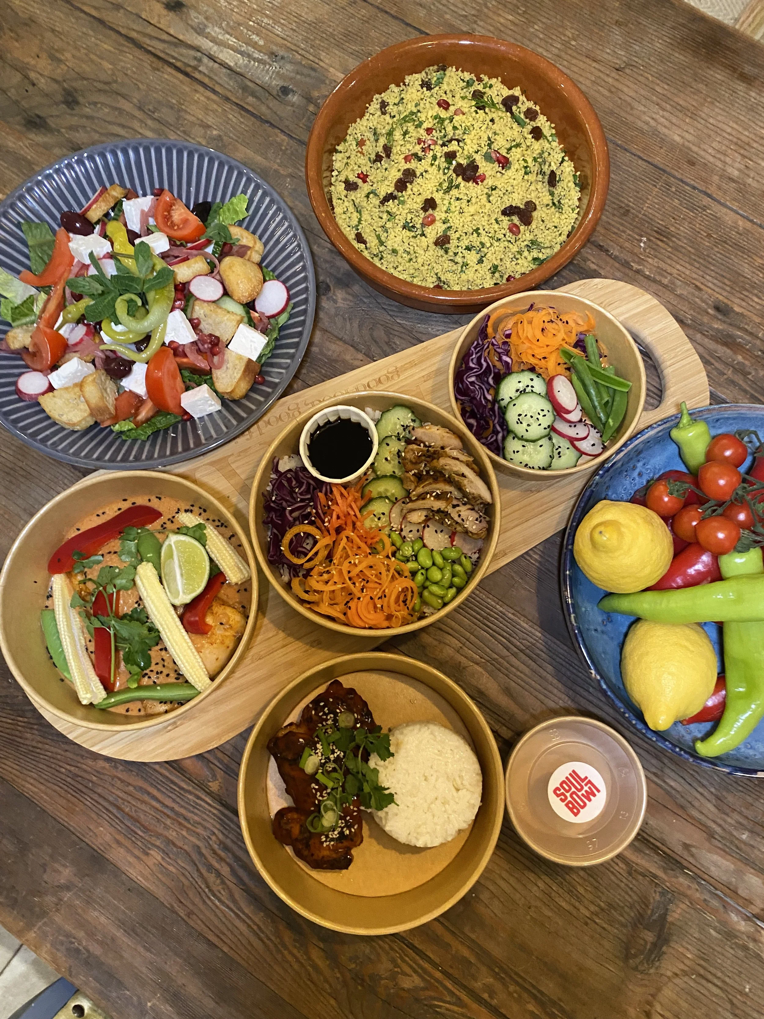 A variety of colorful salads and dishes on a wooden table, including rice, vegetables, and meat dishes.