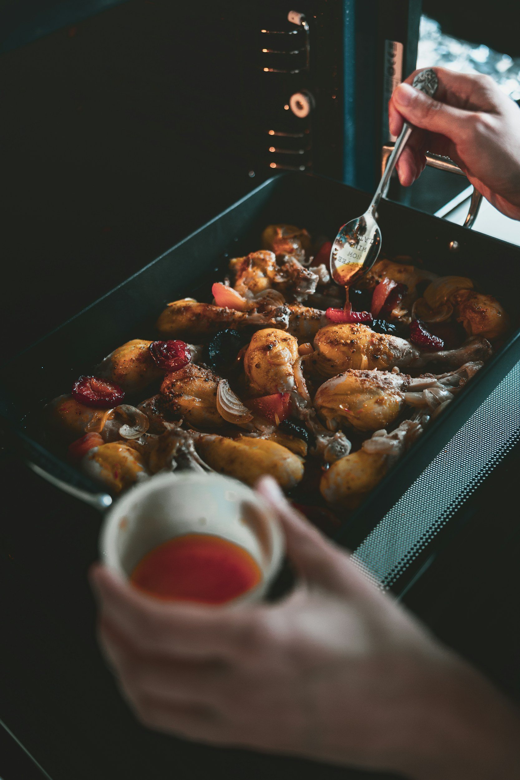 A person holding a small bowl of red dipping sauce over a baking tray of chicken wings, which are being seasoned with hot sauce. Event catering from Soul Bowl Nottinghamshire