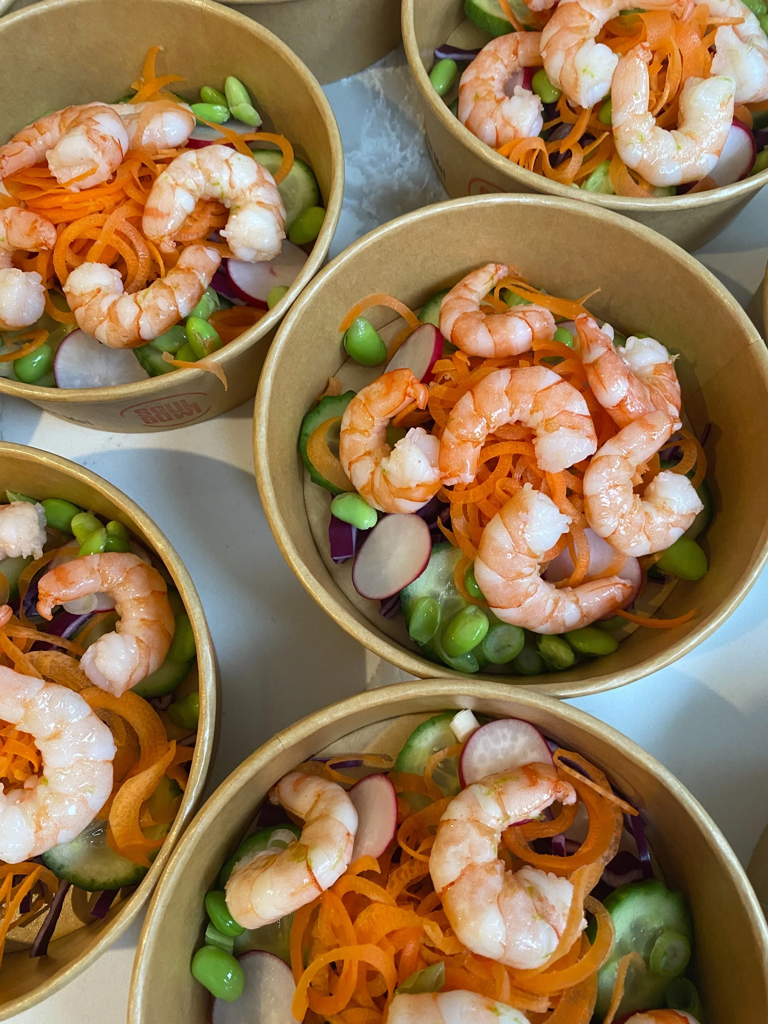 Bowls filled with shrimp, shredded carrots, sliced radishes, green peas, and cucumber slices. poke bowls by Soul Bowl