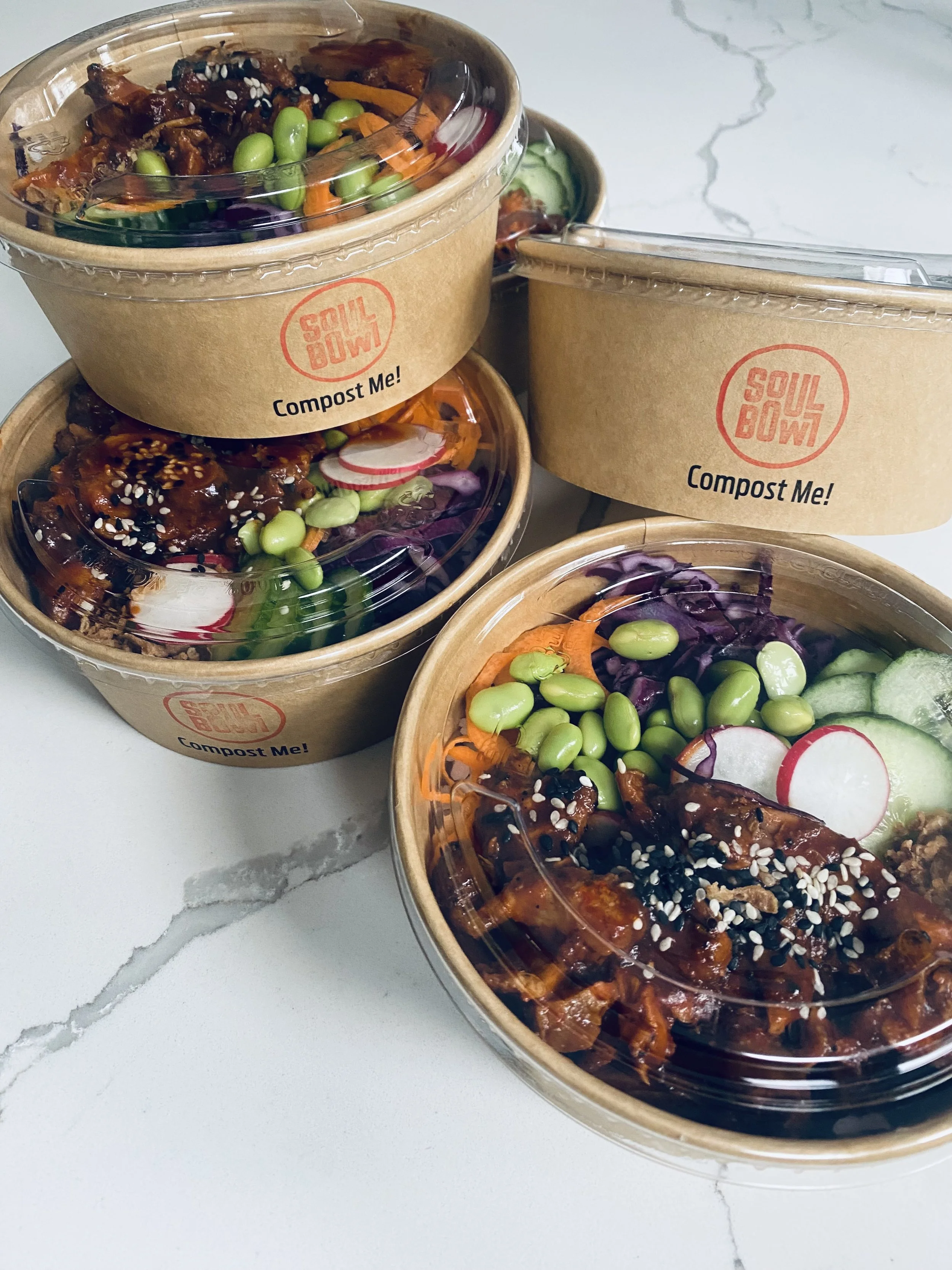 Multiple takeout bowls of Asian-style shredded meat over rice or vegetables, topped with sesame seeds and chopped scallions, placed on a white marble surface.